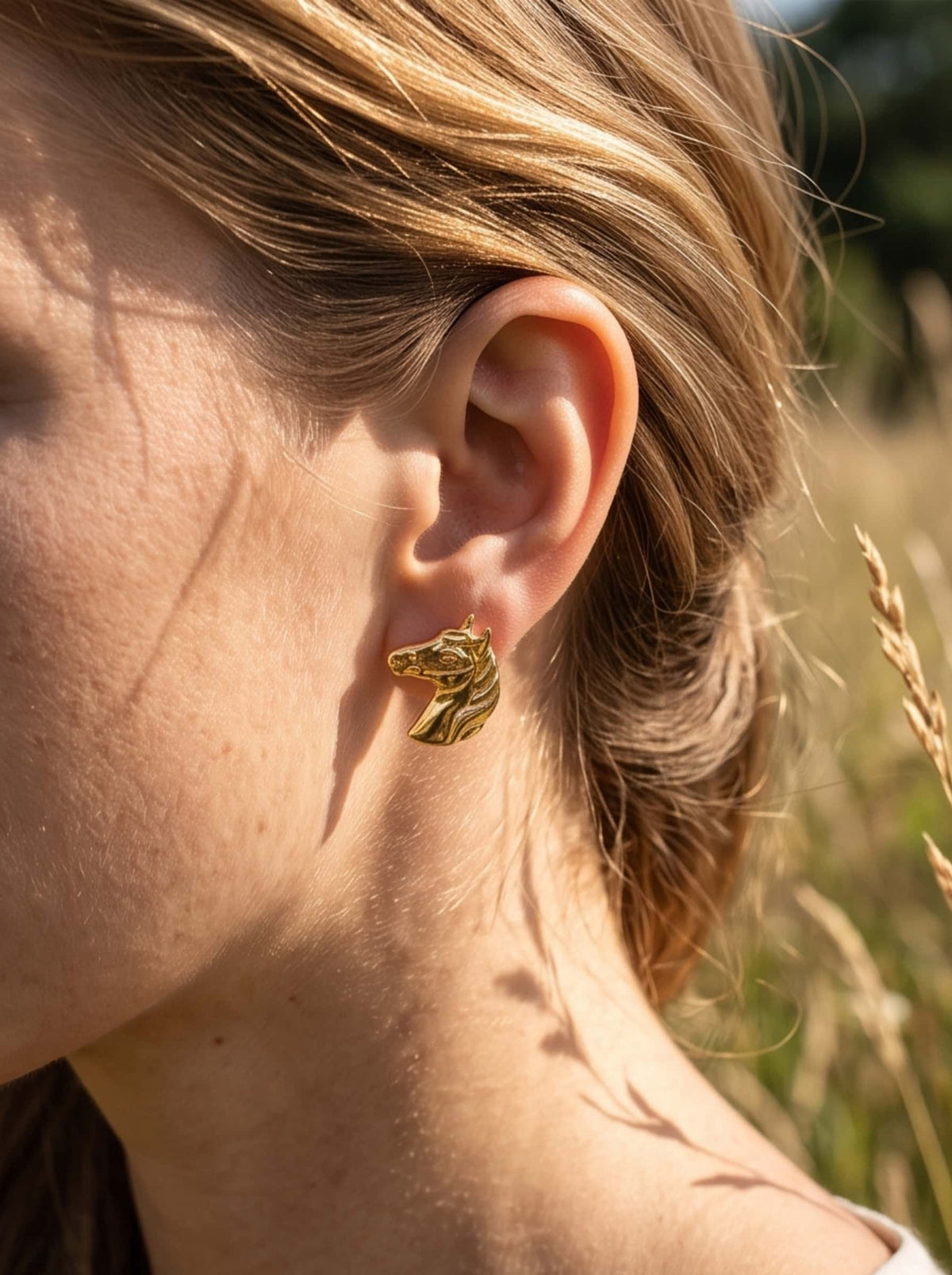 Close-up shot of a model wearing 18K gold plated horse earrings in natural sunlight