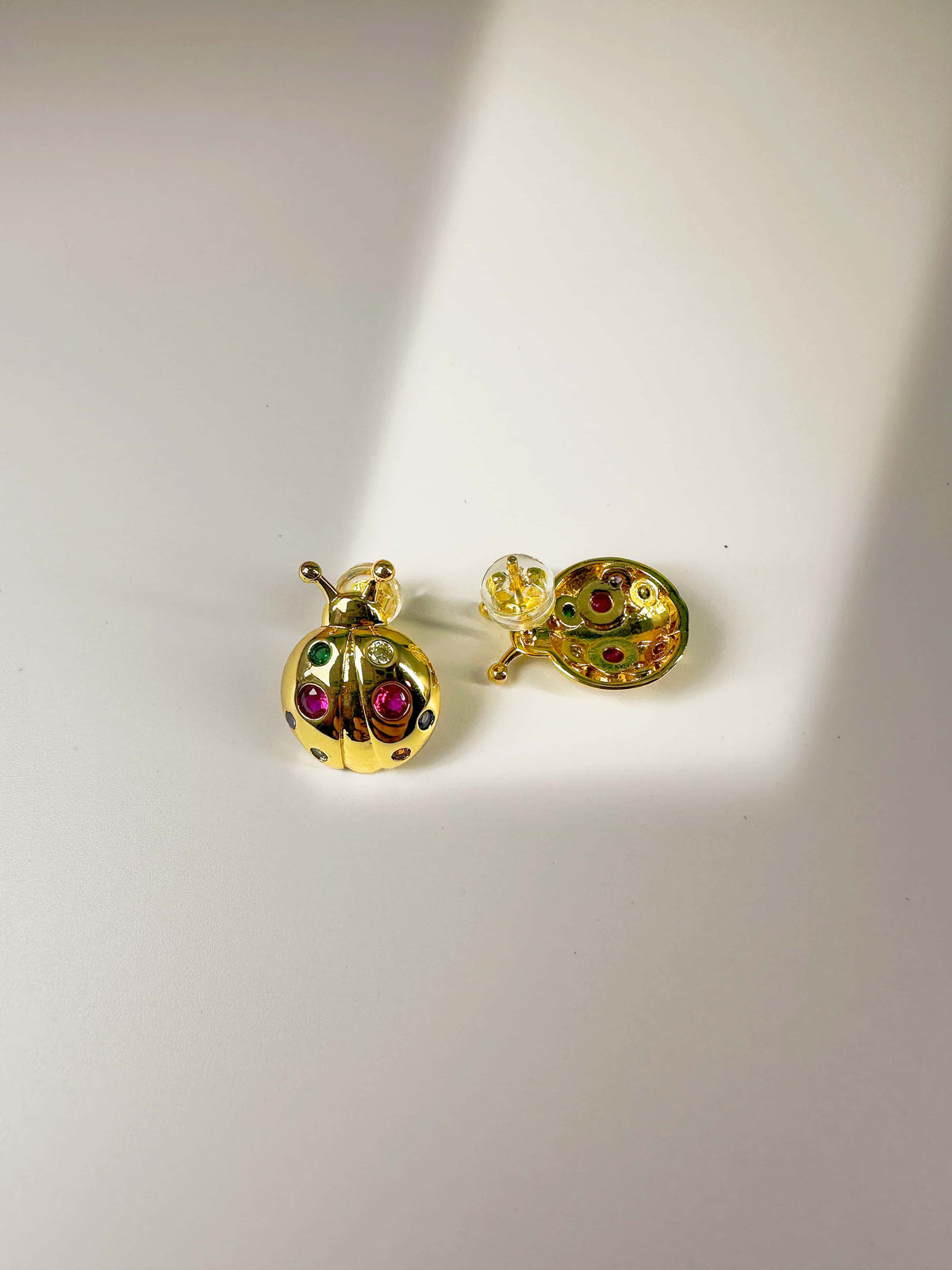 Pair of 18K gold plated ladybug earrings with colorful zirconia stones, displaying the dimensional front design and secure backings on a white surface