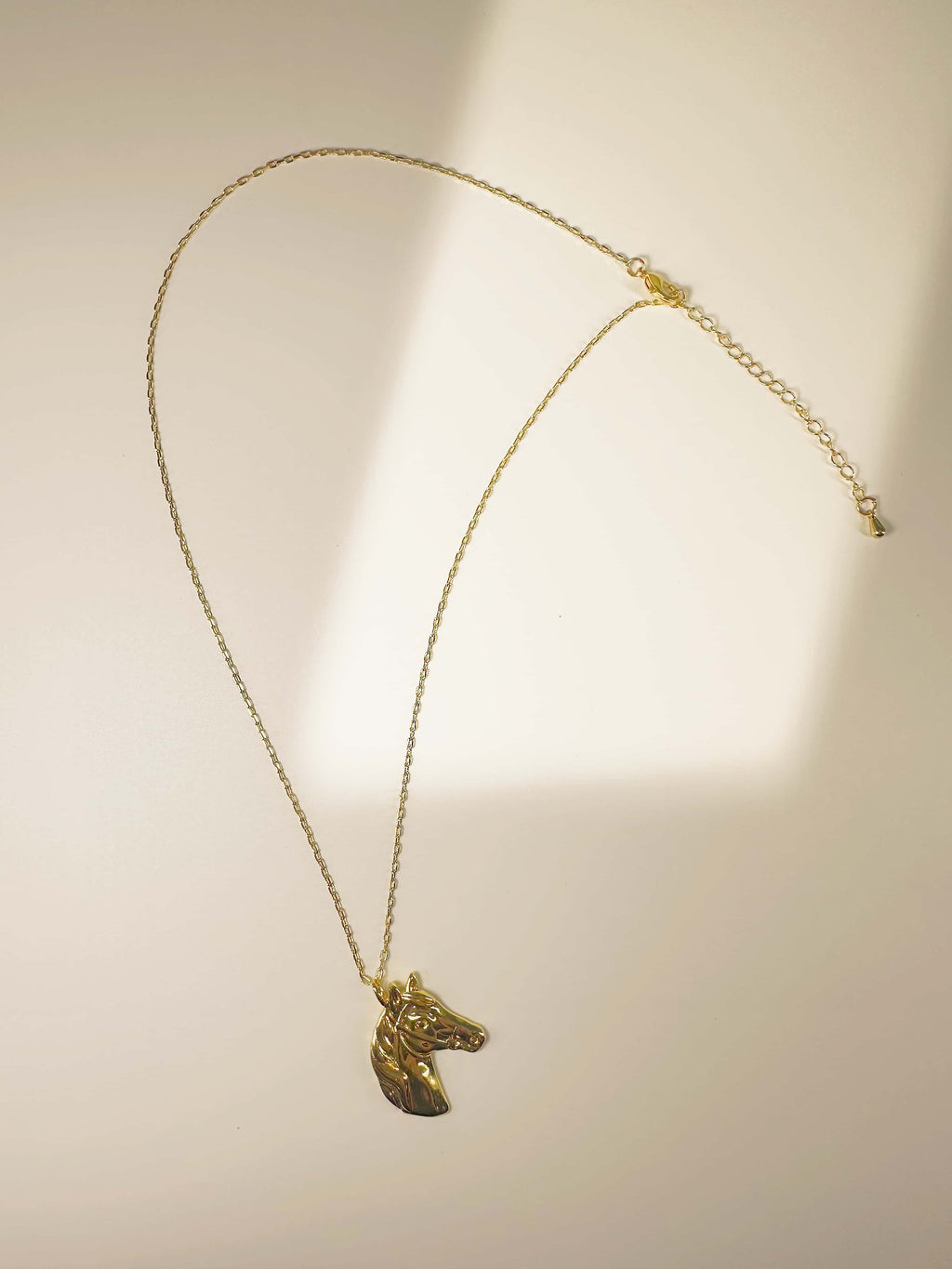 Full view of the gold horse necklace with an adjustable chain and lobster clasp, displayed under soft natural lighting