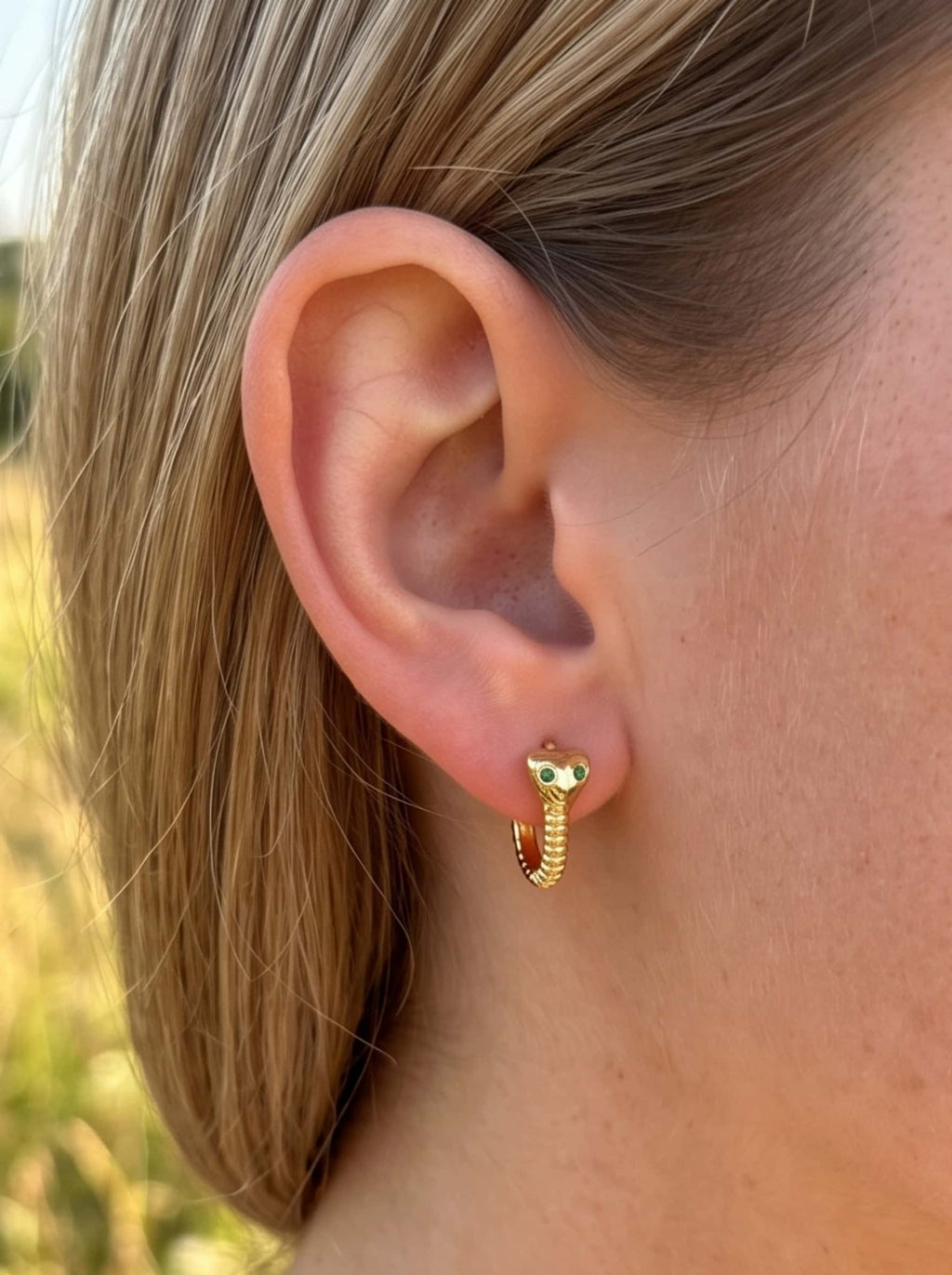 Close-up detail of 18K gold snake earrings with green eyes worn on female earlobe