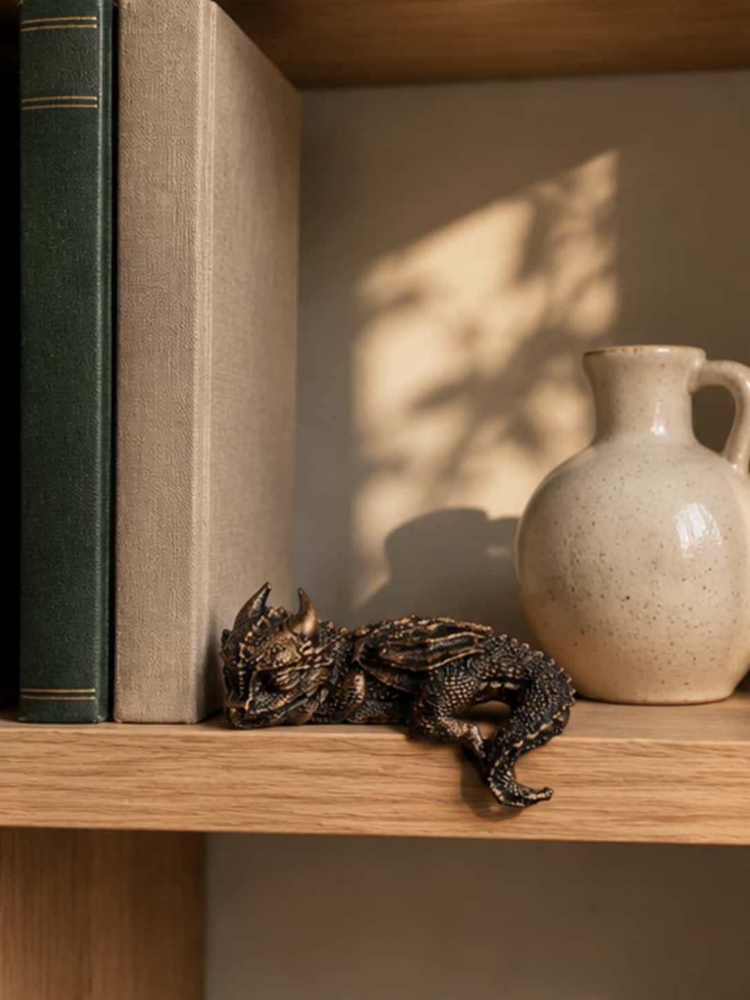 Handcrafted resin dragon figure resting on an oak bookshelf ledge next to classic books and a ceramic vase