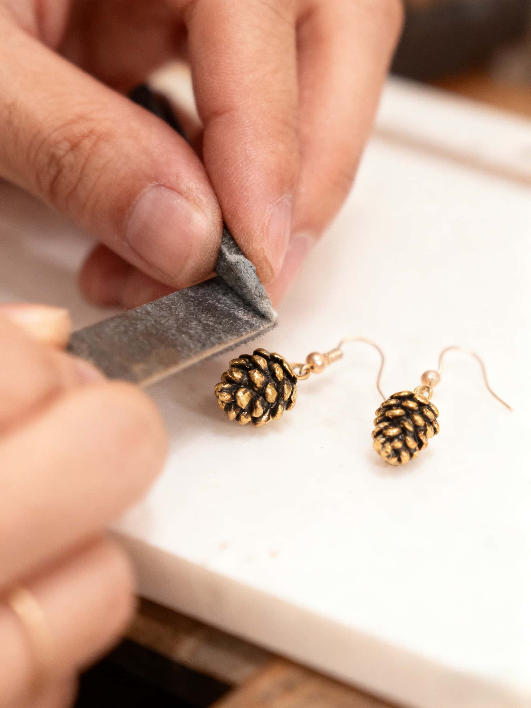 Gold earrings being filed with a sanding block on a white surface.