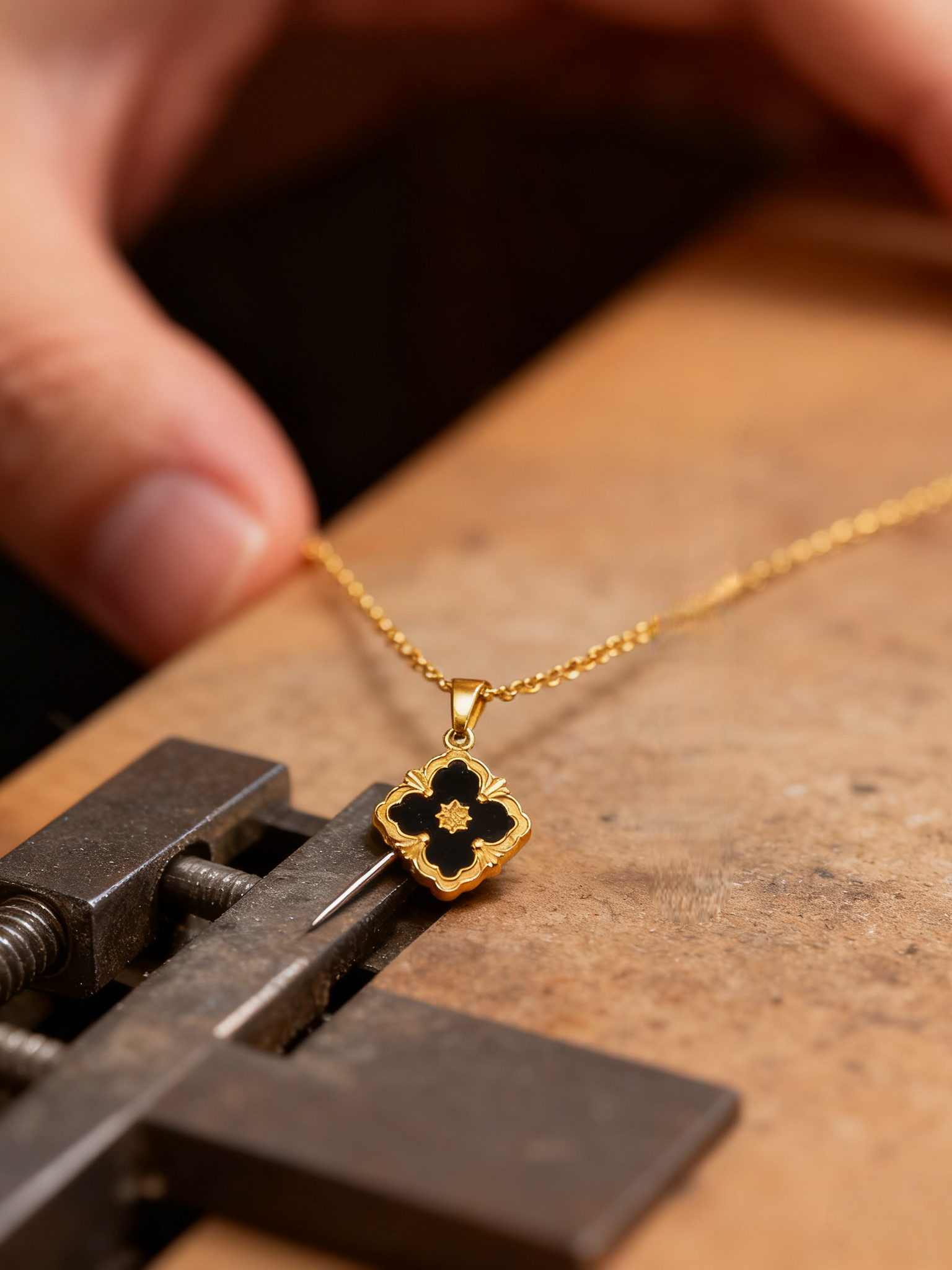 Gold necklace with a clover-shaped pendant on a wooden surface.