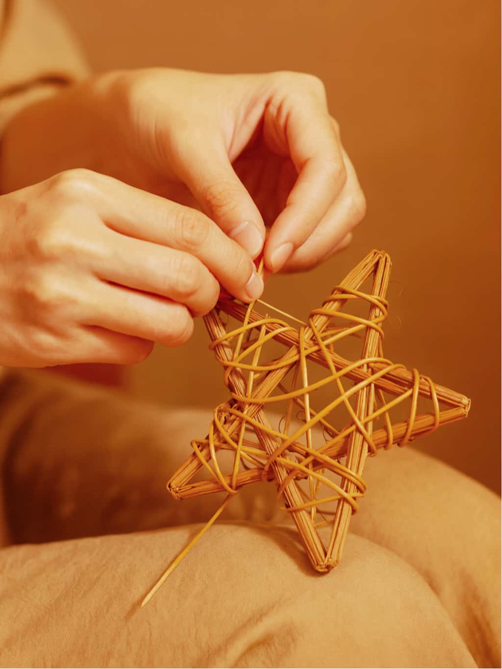 Person crafting a star-shaped woven object with a warm, brown background
