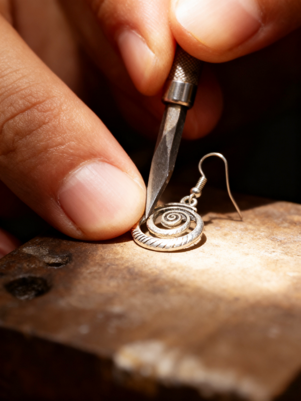 Silver earring being worked on with a tool by a craftsman.