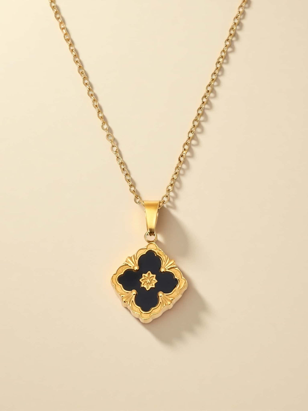 Gold necklace with a black clover pendant on a beige background