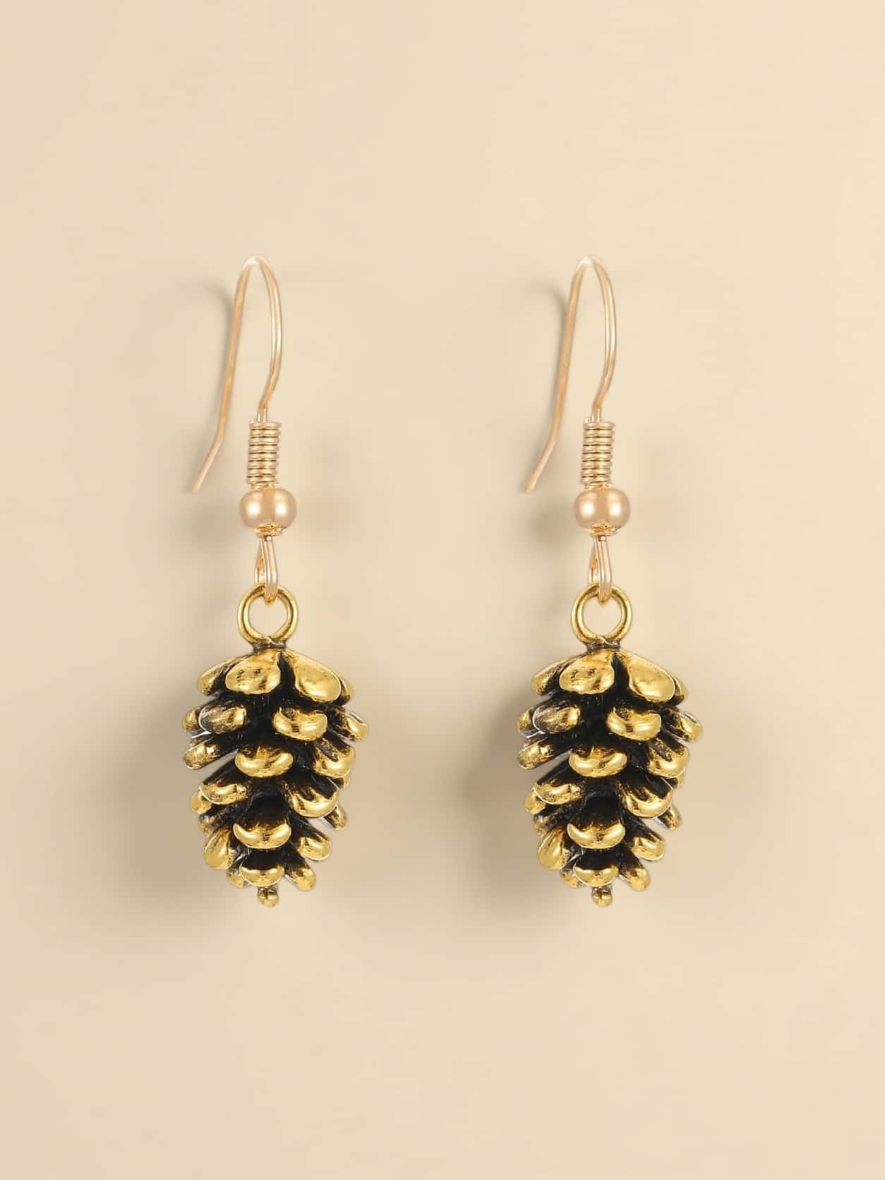 Pine cone-shaped earrings with gold and black finish on a beige background