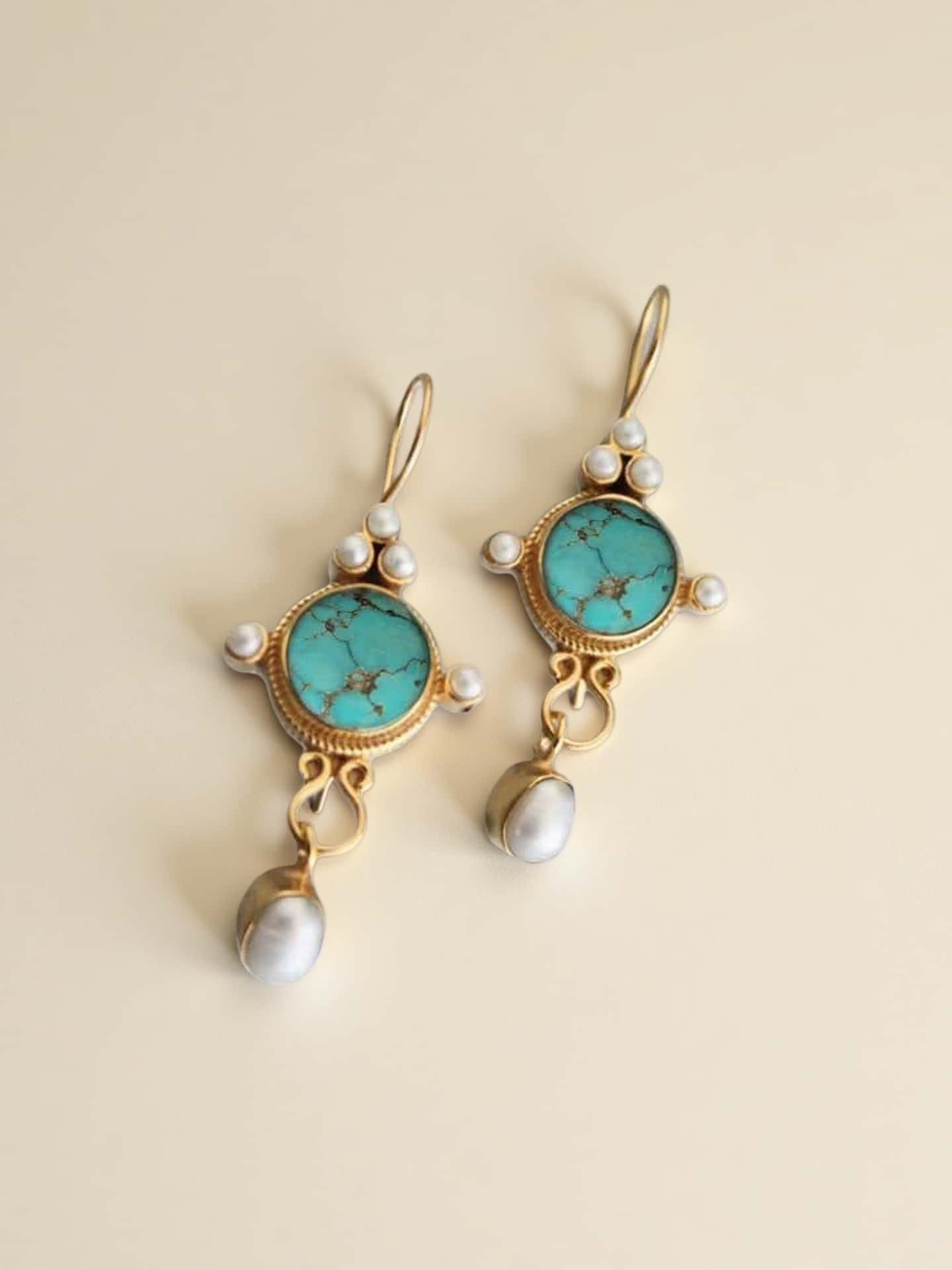 Pair of earrings with turquoise stones and pearl drops on a beige background