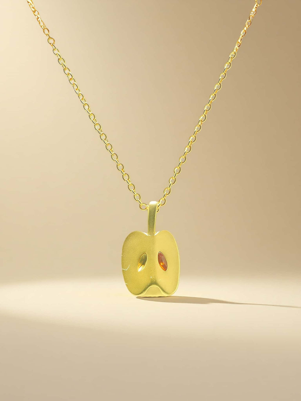Gold apple-shaped pendant necklace on a beige background