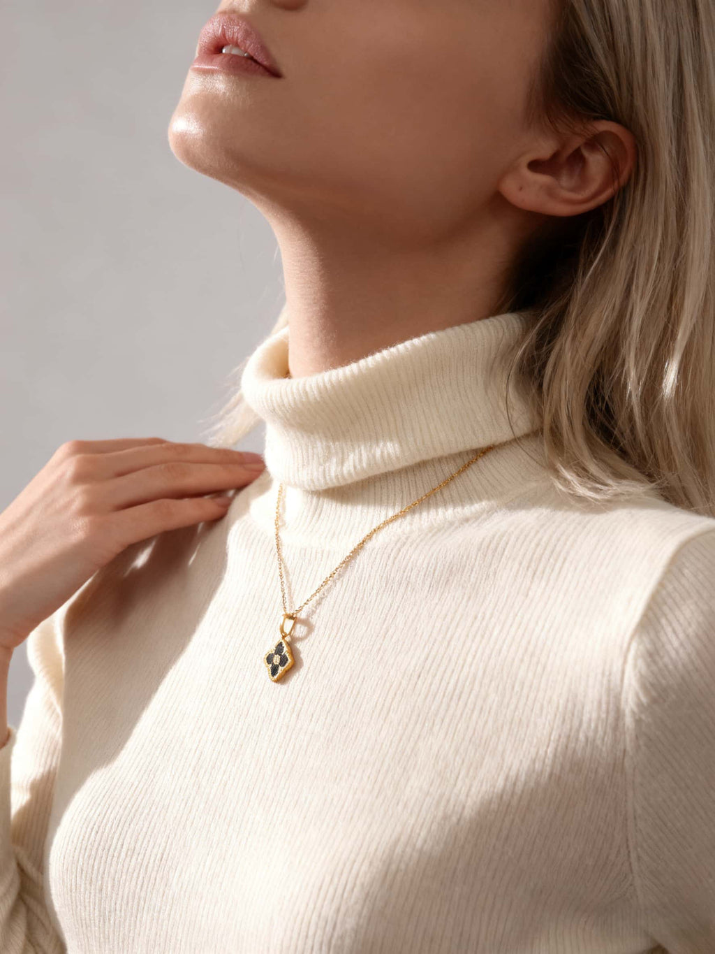 Person wearing a gold necklace with a pendant against a neutral background