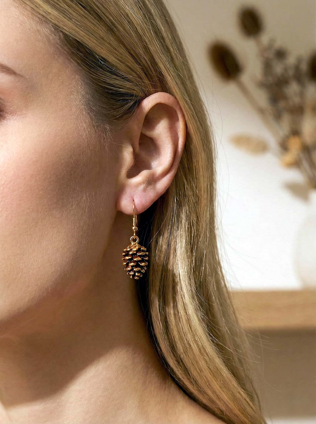 Close-up of a person wearing a pine cone-shaped earring with a blurred background.