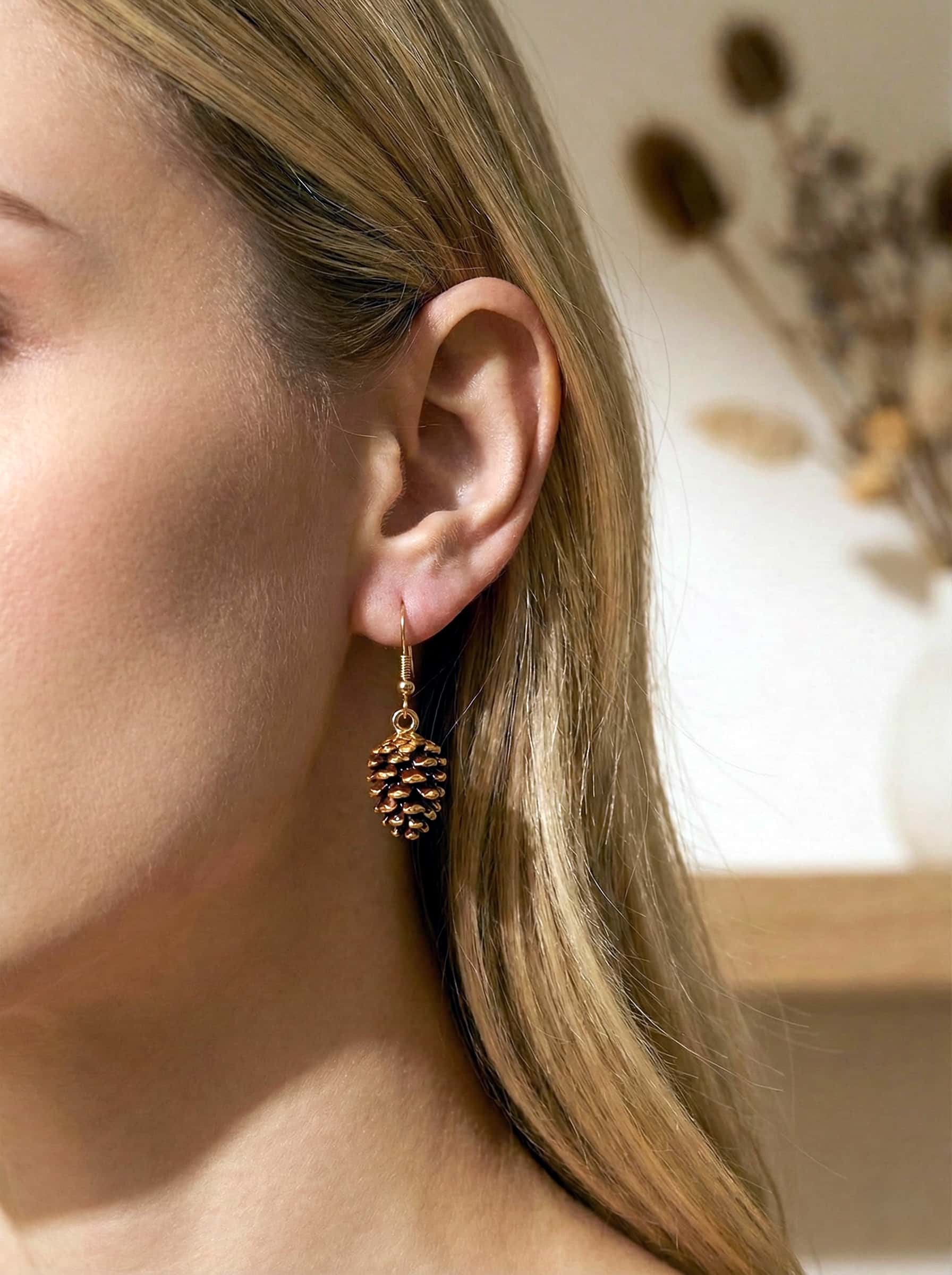 Close-up of a person wearing a pine cone-shaped earring with a blurred background.