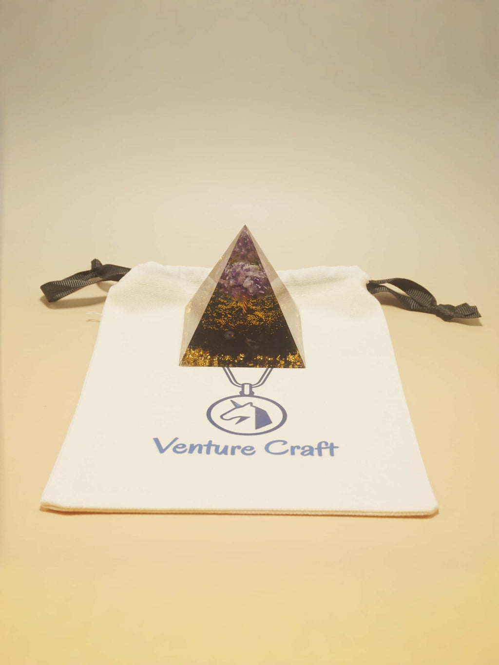 Triangle-shaped pendant on a 'Venture Craft' branded bag against a beige background