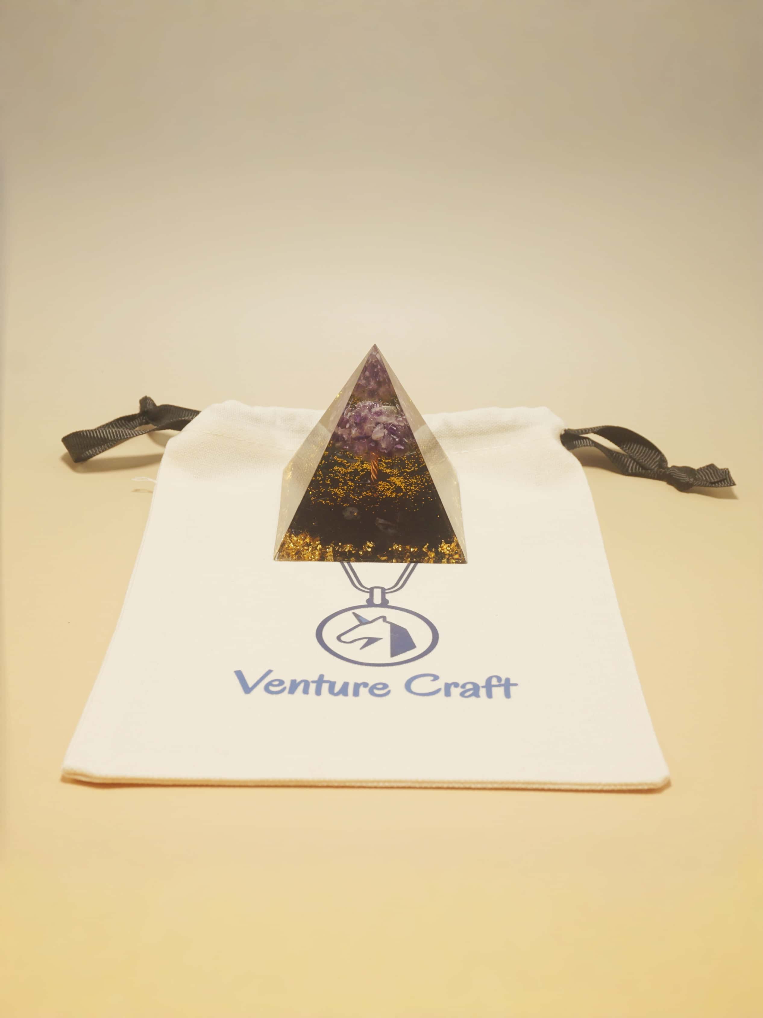 Triangle-shaped pendant on a 'Venture Craft' branded bag against a beige background