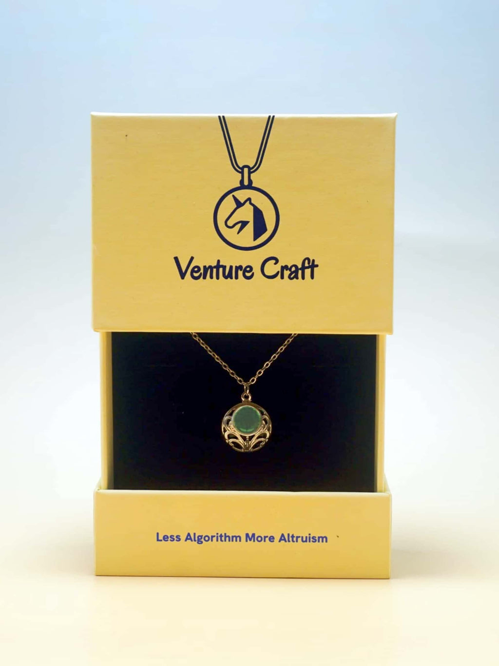 Gold necklace with a pendant in a yellow Venture Craft box on a light blue background