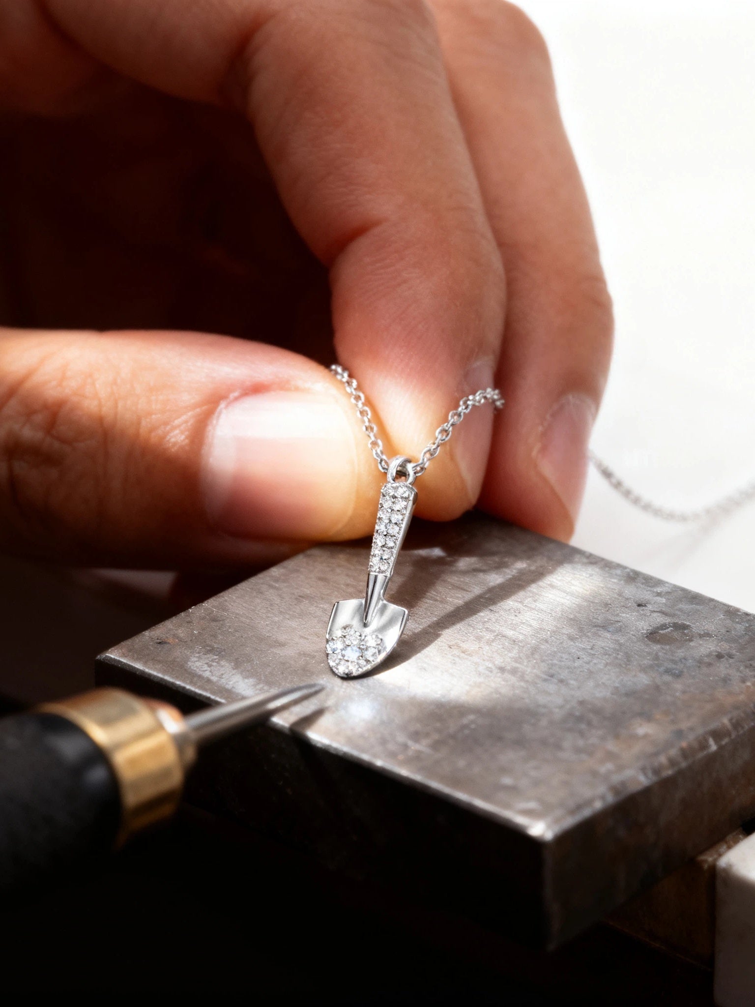 Close-up of a hand holding a silver necklace with a pendant on a workbench.