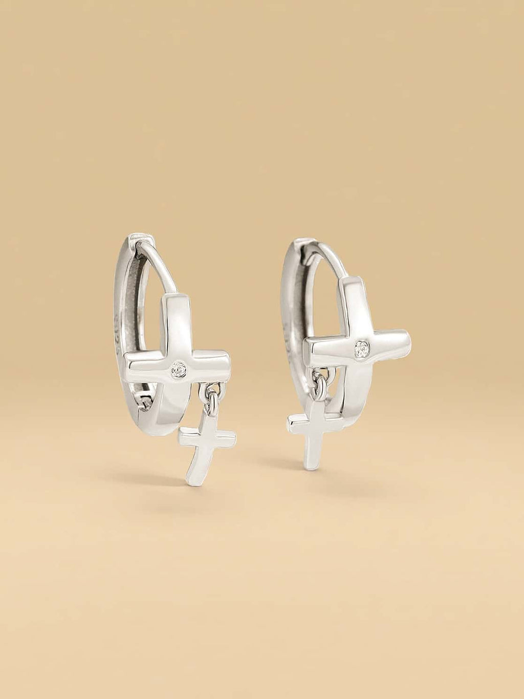 Silver hoop earrings with cross charms on a beige background