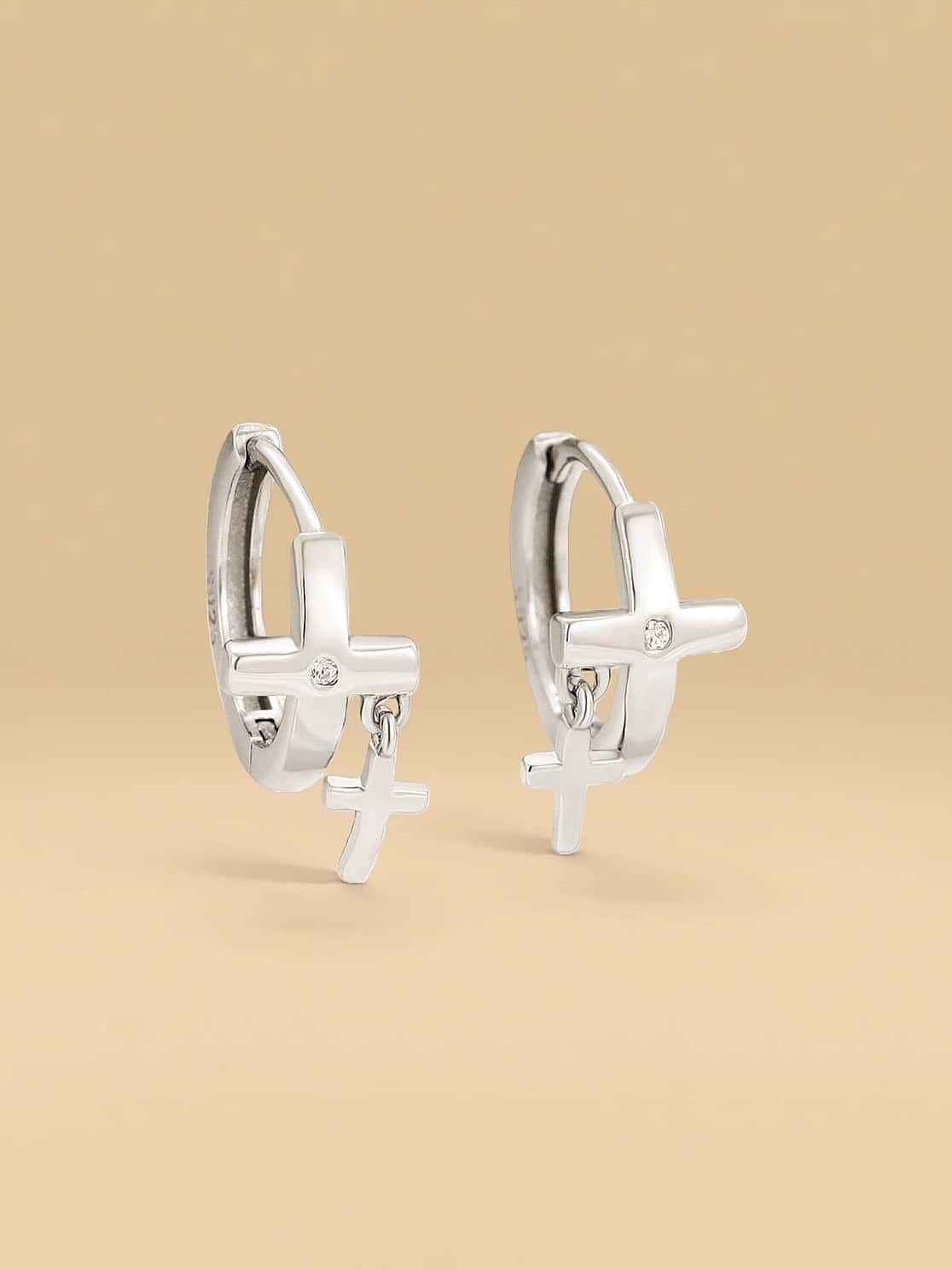 Silver hoop earrings with cross charms on a beige background