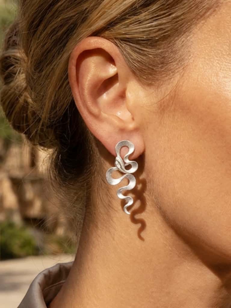Close-up of a person wearing silver snake earrings with a blurred outdoor background