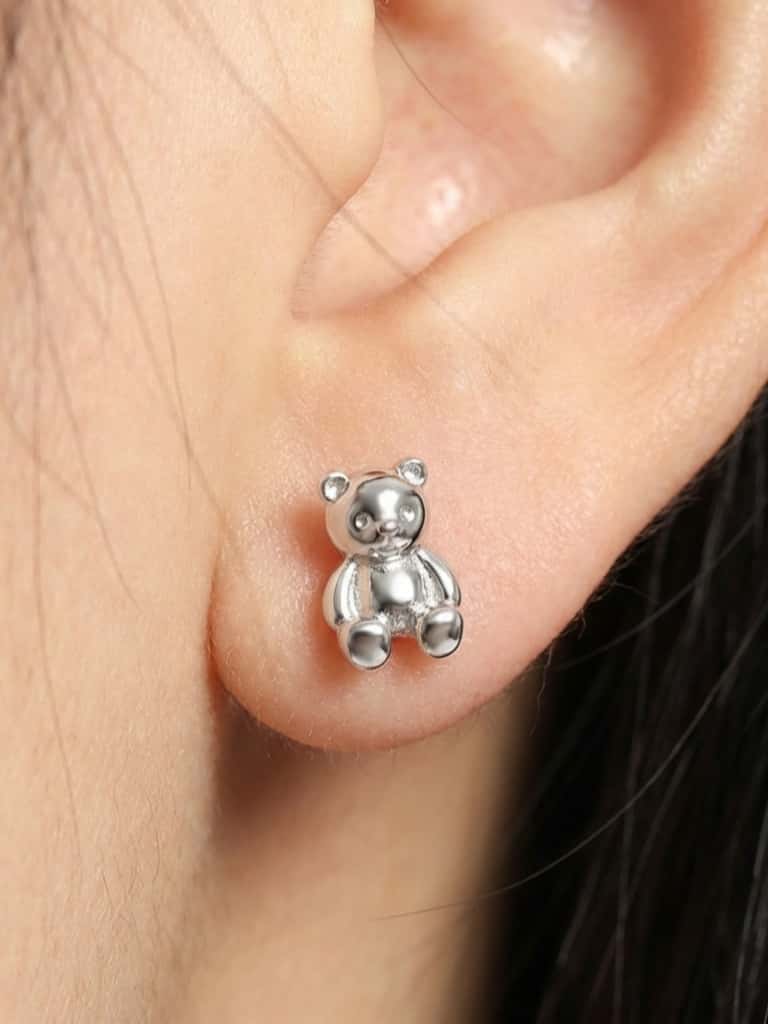 Silver teddy bear earring worn on an ear