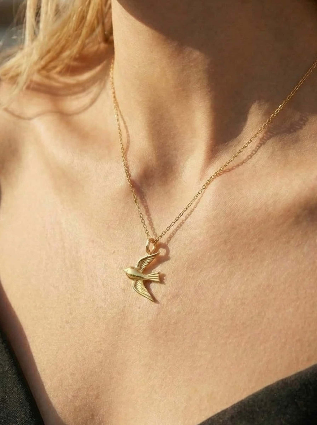 Gold necklace with a swallow pendant on a model's neck