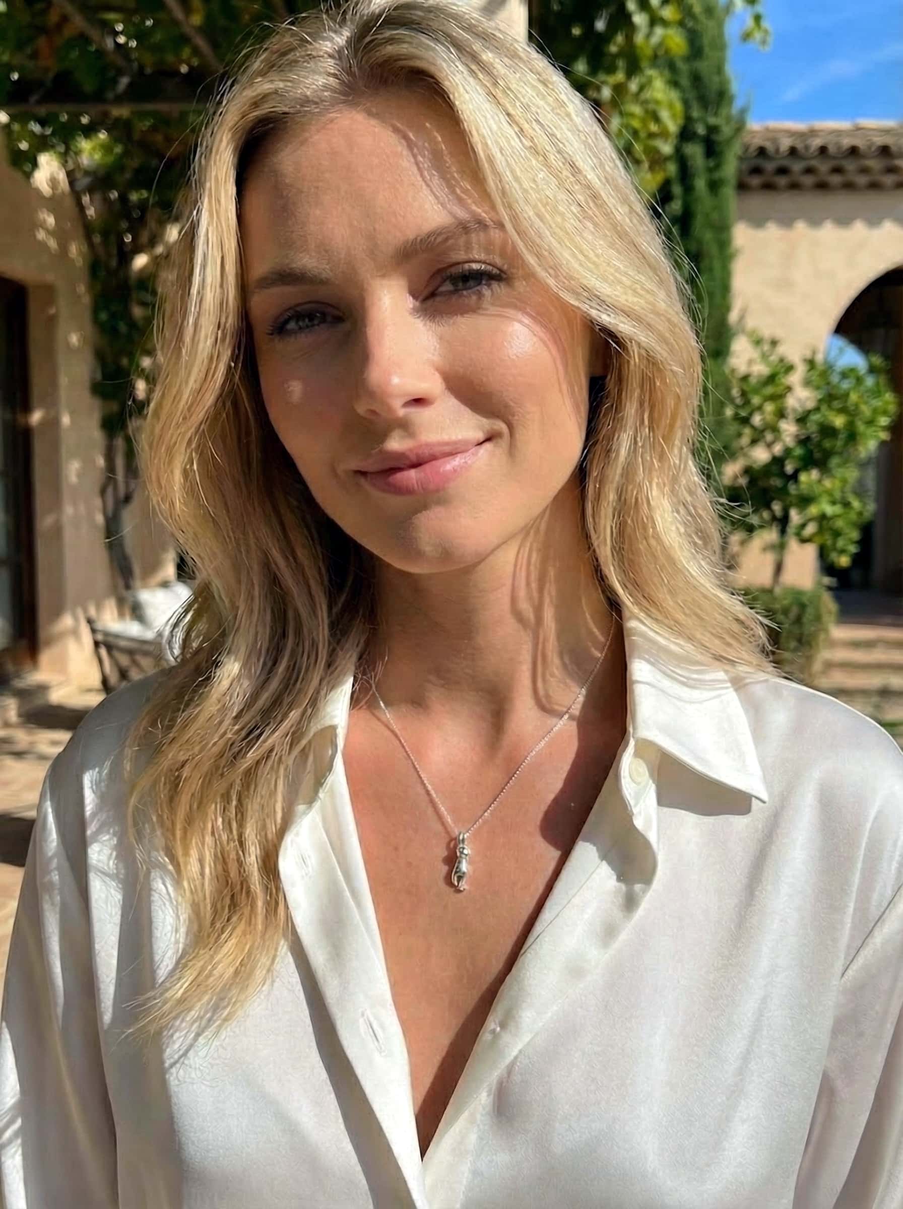 Woman wearing silver cat-shaped pendant with a blurred outdoor background