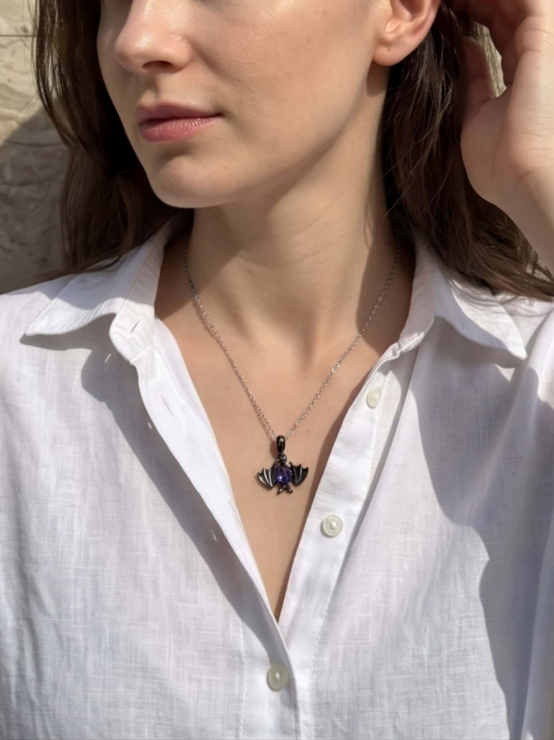 Elegant woman wearing a bat necklace silver pendant styled over a classic white button-down shirt