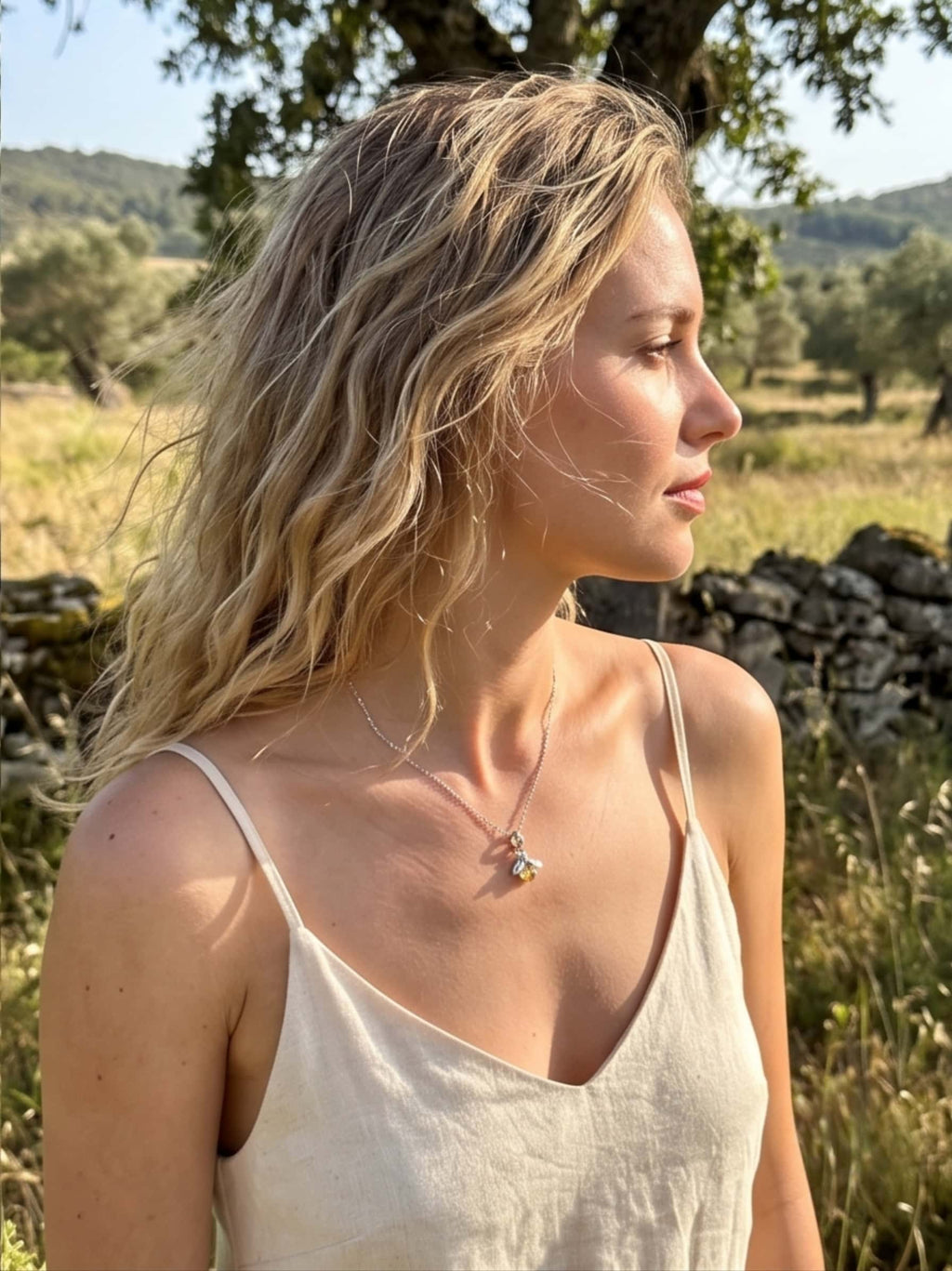 Profile view of a woman outdoors wearing a radiant bee necklace gold crystal pendant that catches the beautiful summer afternoon light