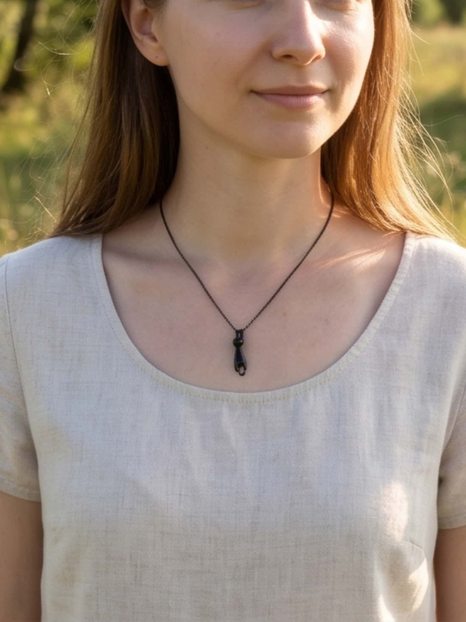 A smiling woman wearing a minimalist black cat necklace paired with a light beige casual linen dress
