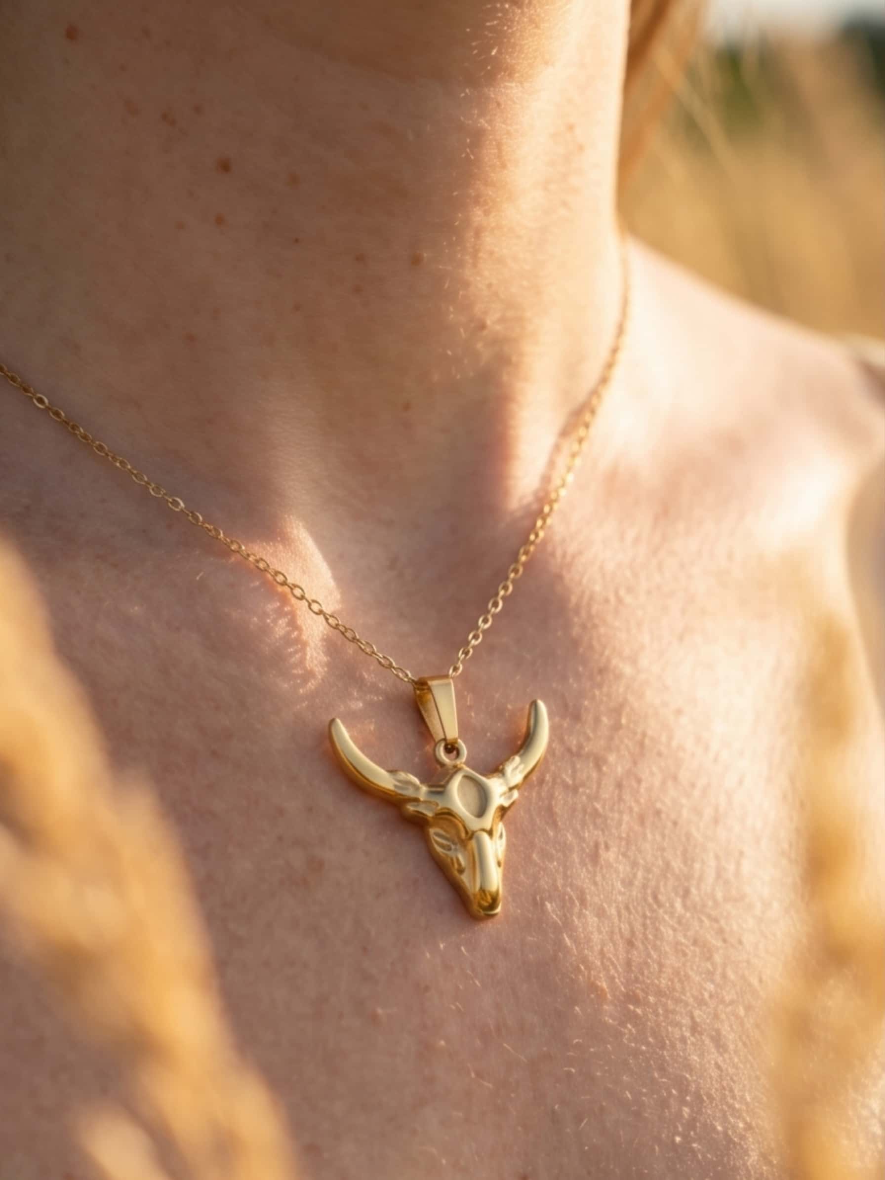 Close up detail of the golden bull necklace resting on a collarbone, highlighting the smooth 18K gold finish