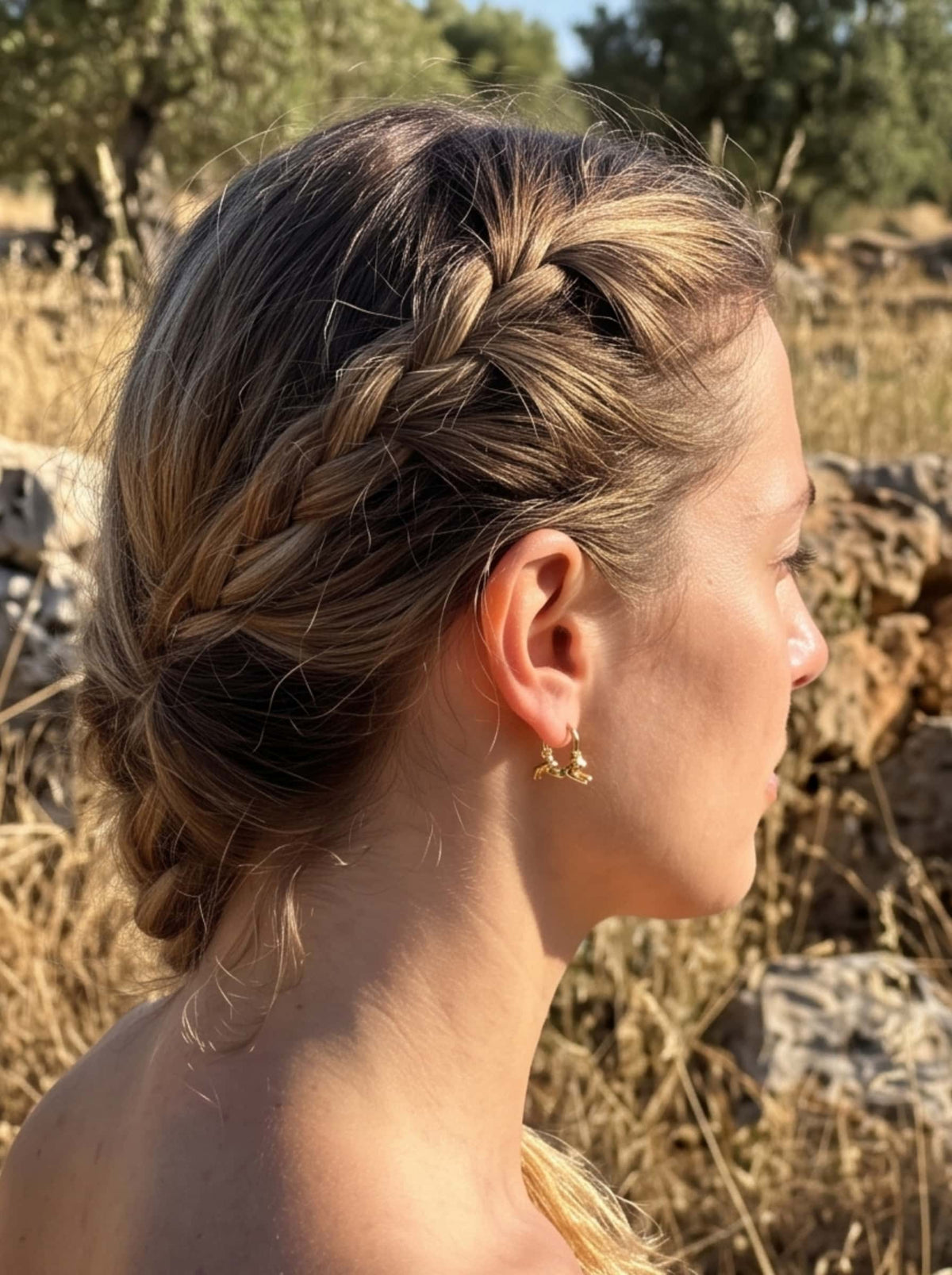Lifestyle portrait of a woman with braided hair wearing gold cat hoop earrings in golden hour sunlight