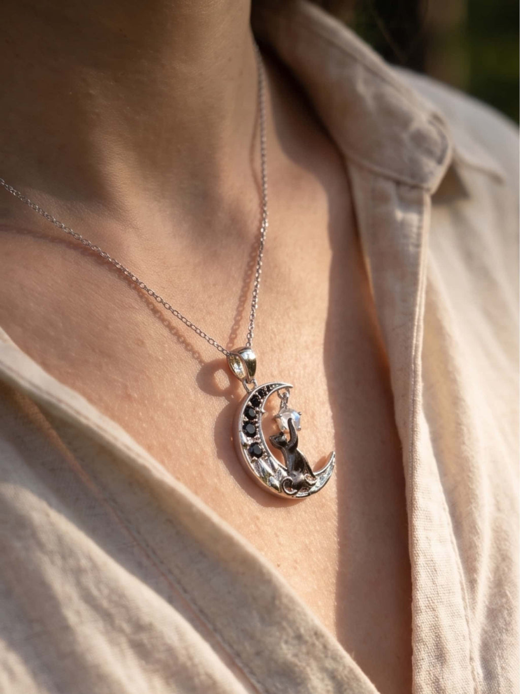 A delicate silver cat moon necklace worn by a woman, glowing in natural outdoor sunlight