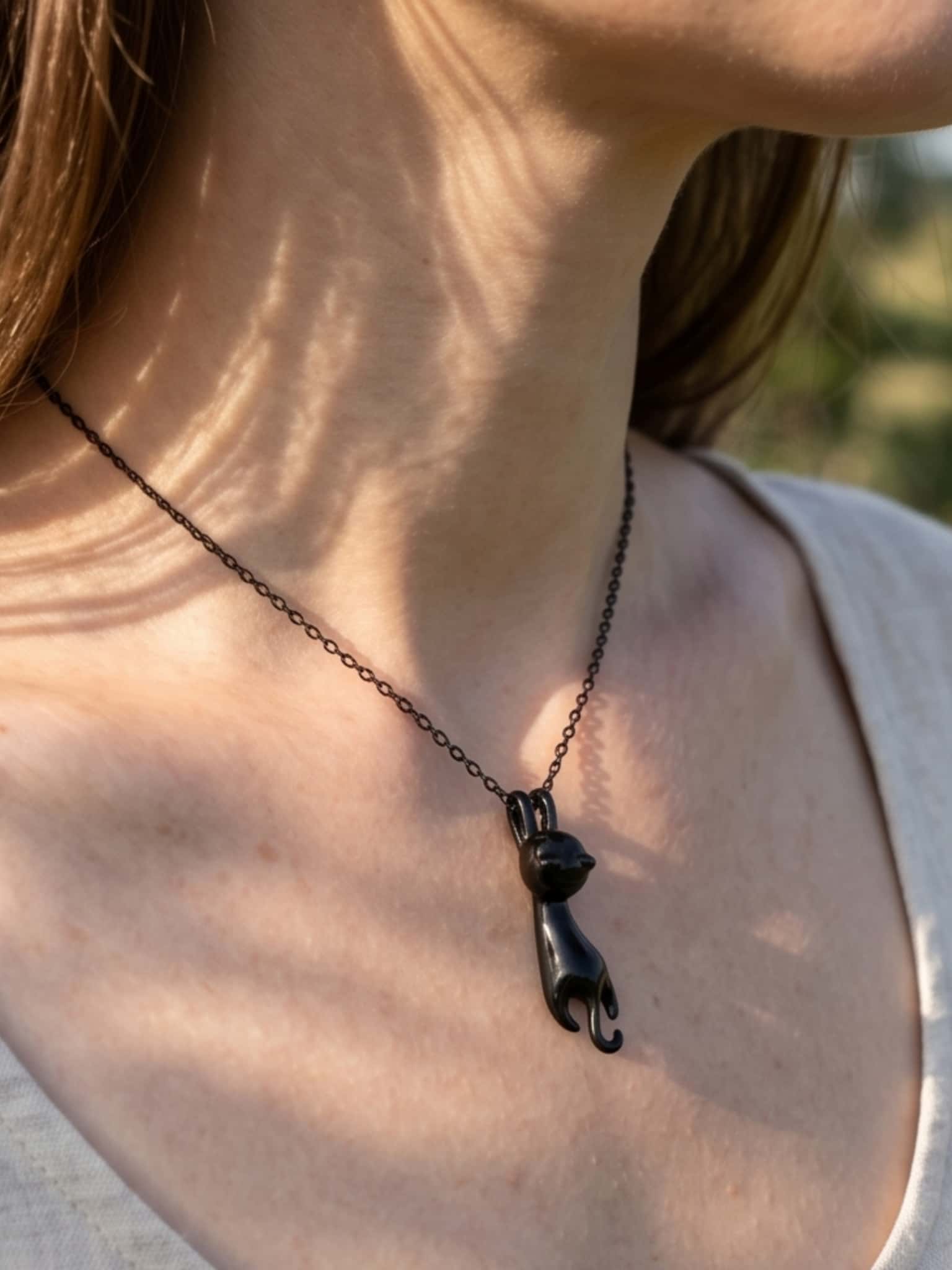 A delicate black cat necklace for women resting beautifully on a model's collarbone under warm sunlight
