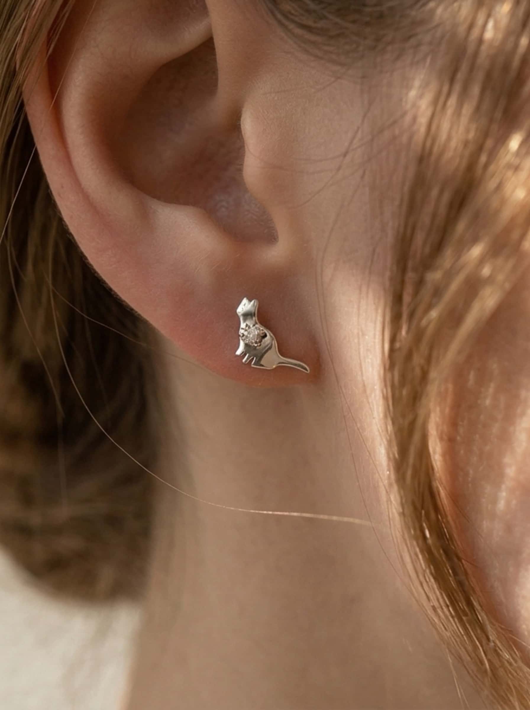 Close-up profile of a woman wearing delicate cat stud earrings made of silver and sparkling zircon