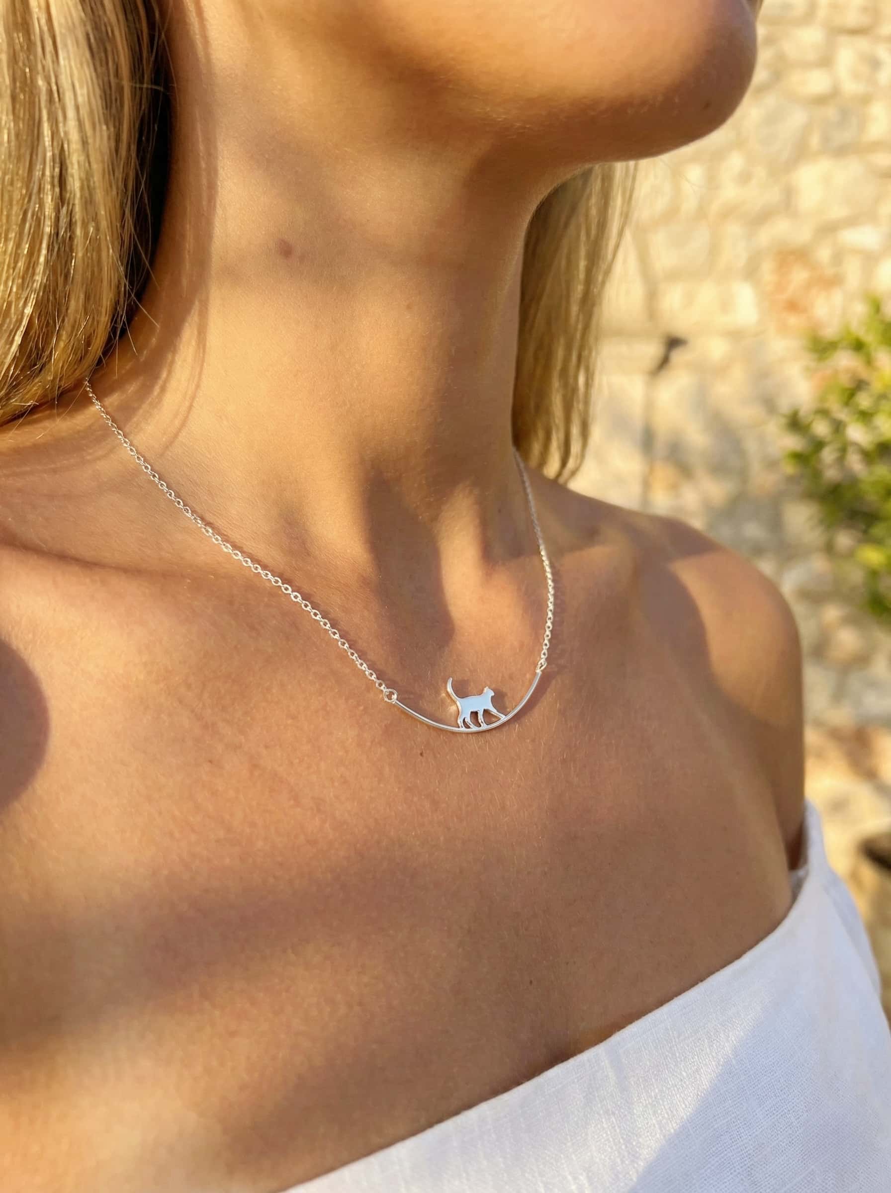 Necklace with a small cat pendant worn by a person outdoors