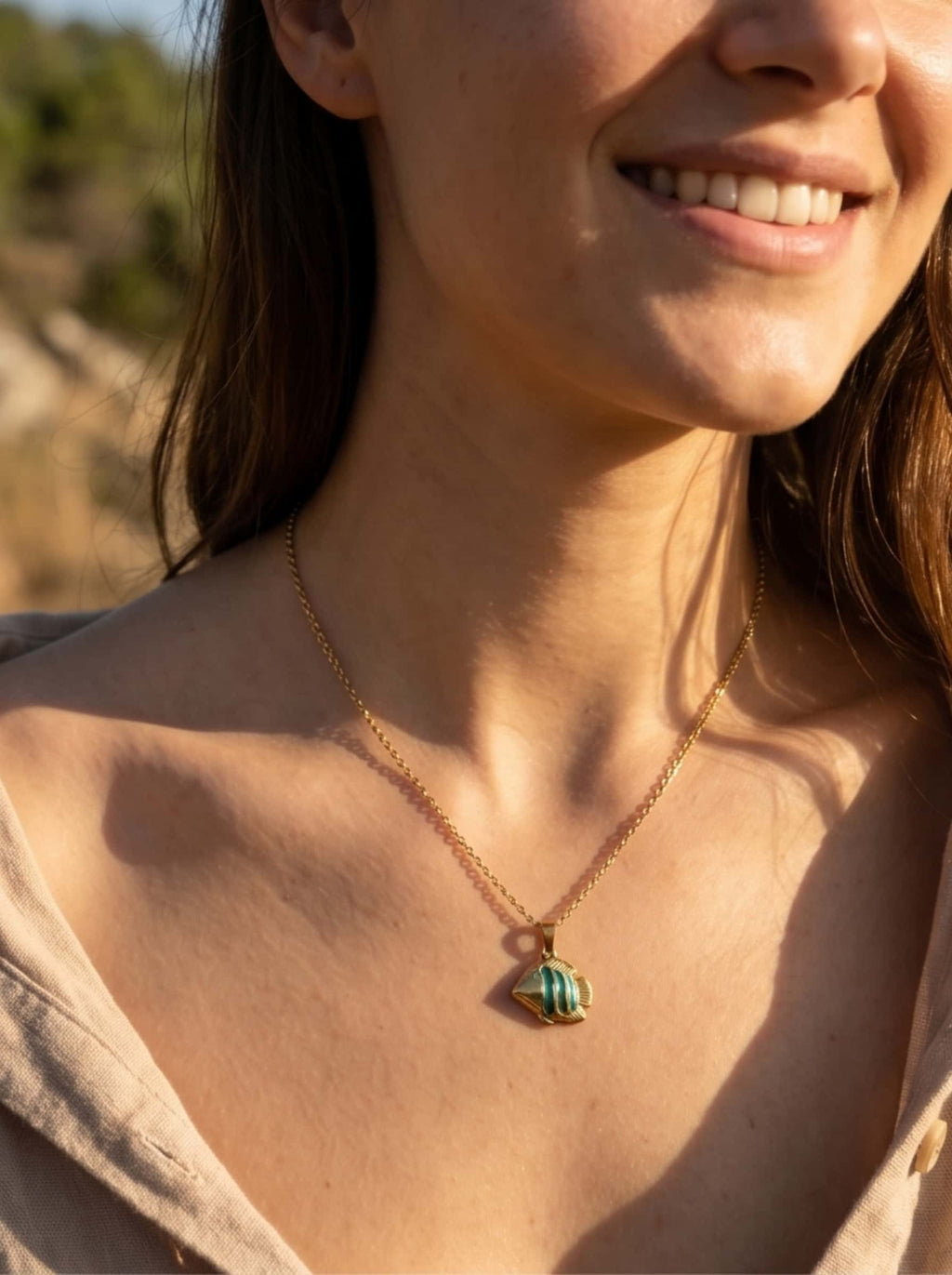 A portrait of a smiling female model wearing the vintage nature-inspired gold fish necklace, showcasing a minimalist clean girl aesthetic under warm evening sunlight