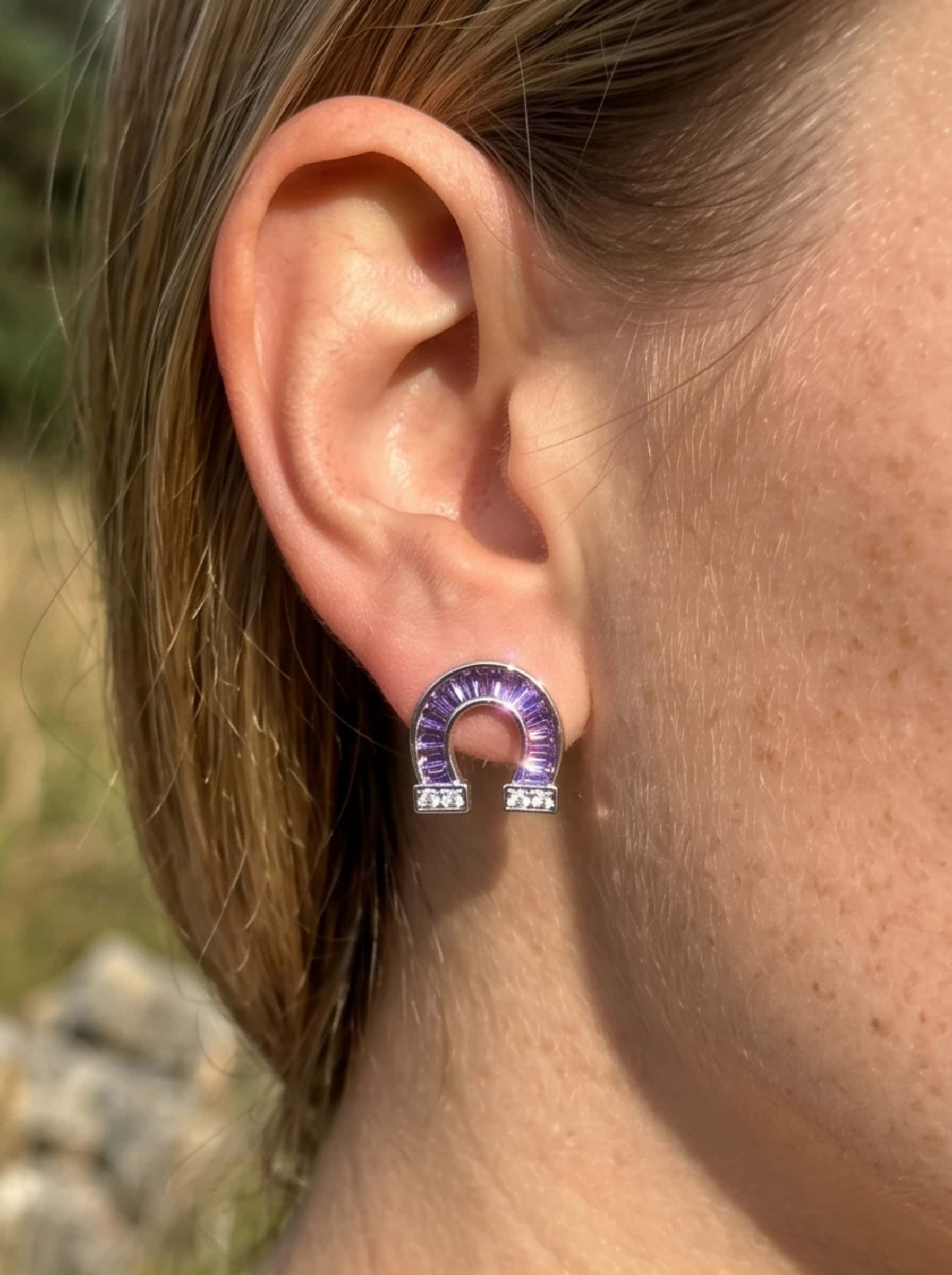 Macro close-up shot of the amethyst and diamond horseshoe earrings sparkling in the sunlight on a model's earlobe