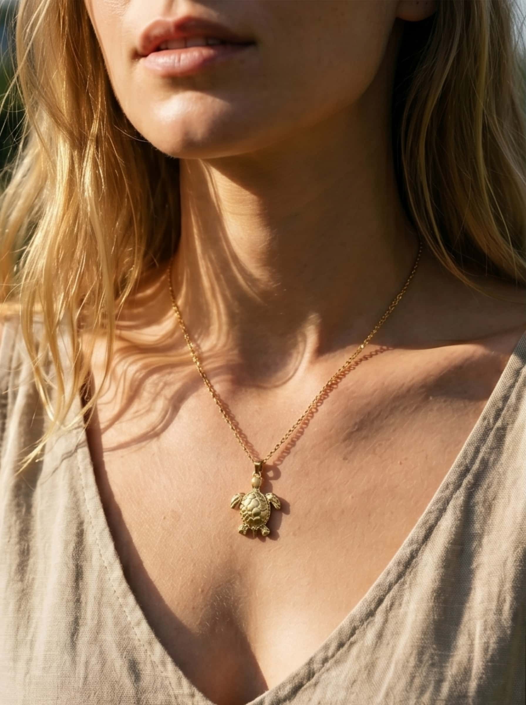 A detailed close-up shot of the intricate shell pattern on the gold sea turtle necklace worn by a model
