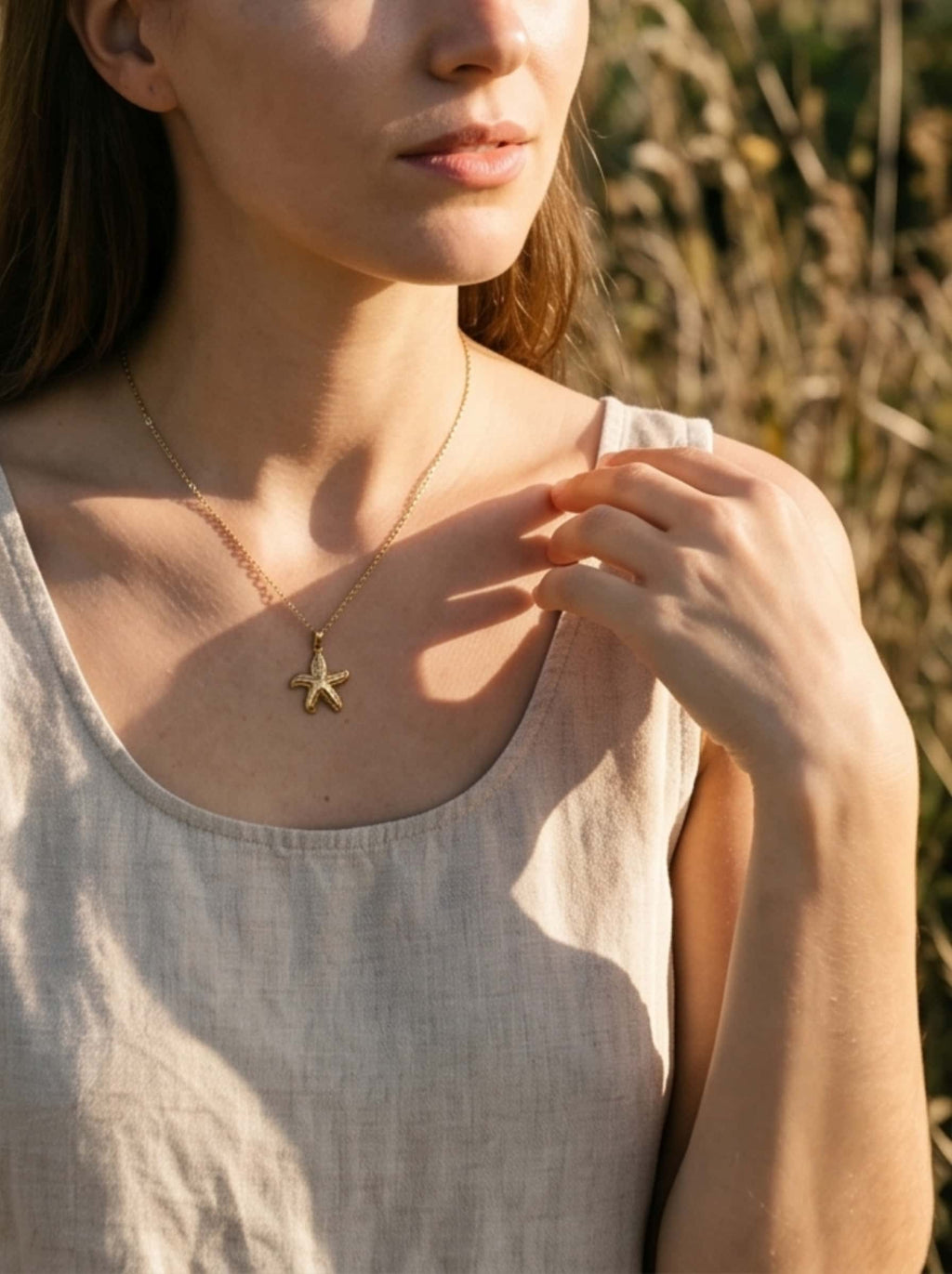 Close-up of an elegant necklace with starfish resting on a woman's collarbone, capturing natural golden hour shadows and summer vibes