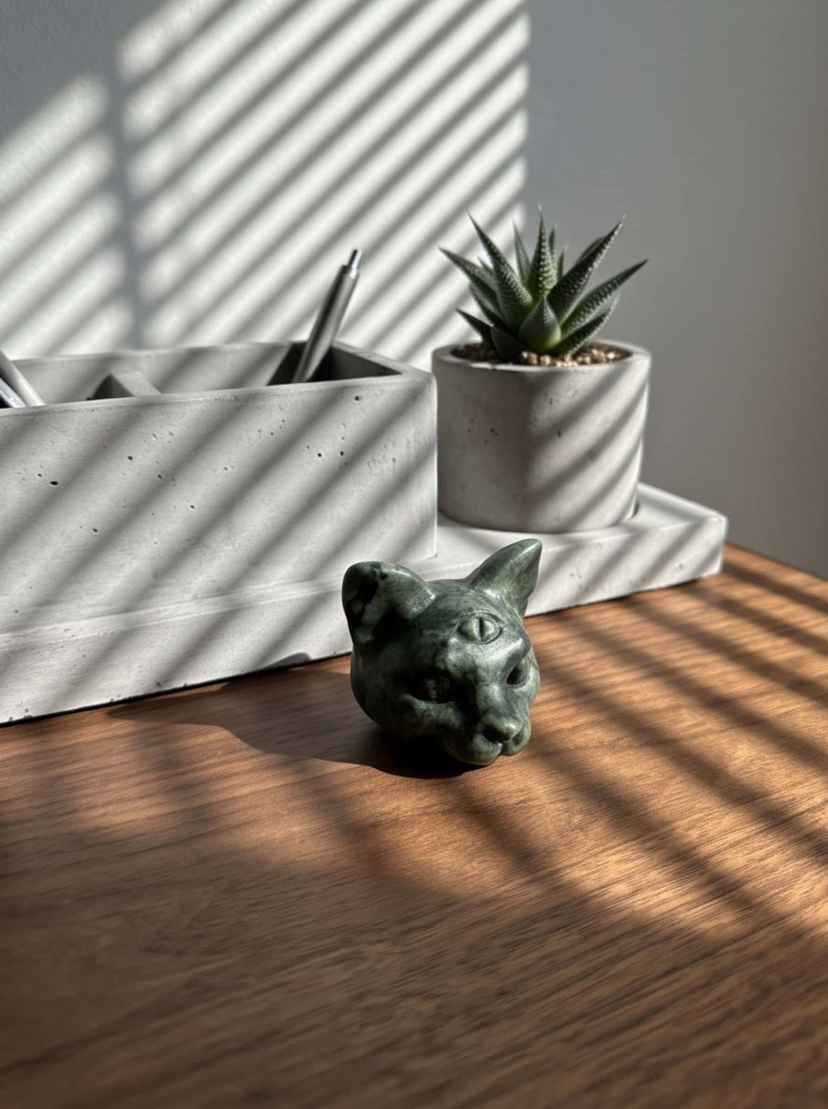 Green gemstone cat figurine displayed on a modern wooden desk beside a concrete pen holder and succulent plant