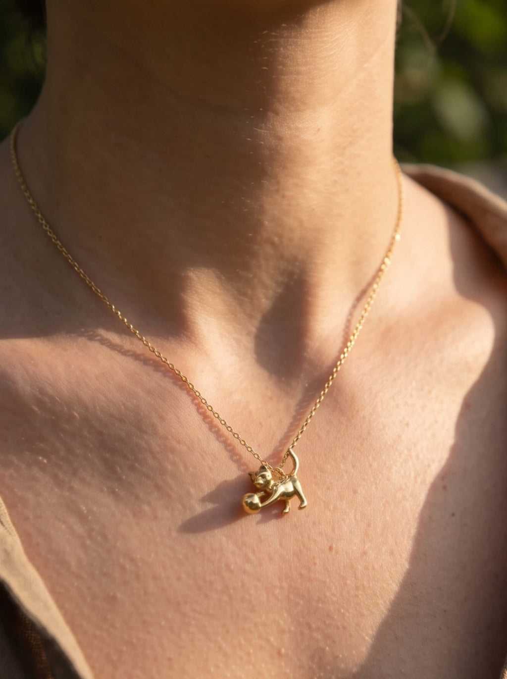 Close-up shot of a model wearing a dainty 18K gold cat necklace with a sculpted cat pendant in warm sunlight