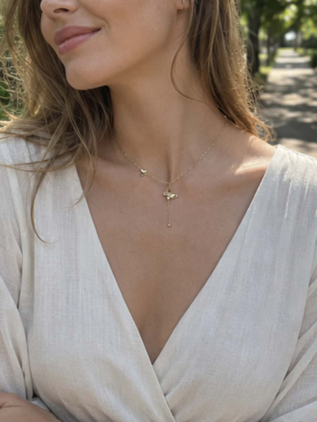 Side view profile of a model showcasing the elegant fit and drape of the dainty butterfly necklace with a white summer outfit in natural daylight
