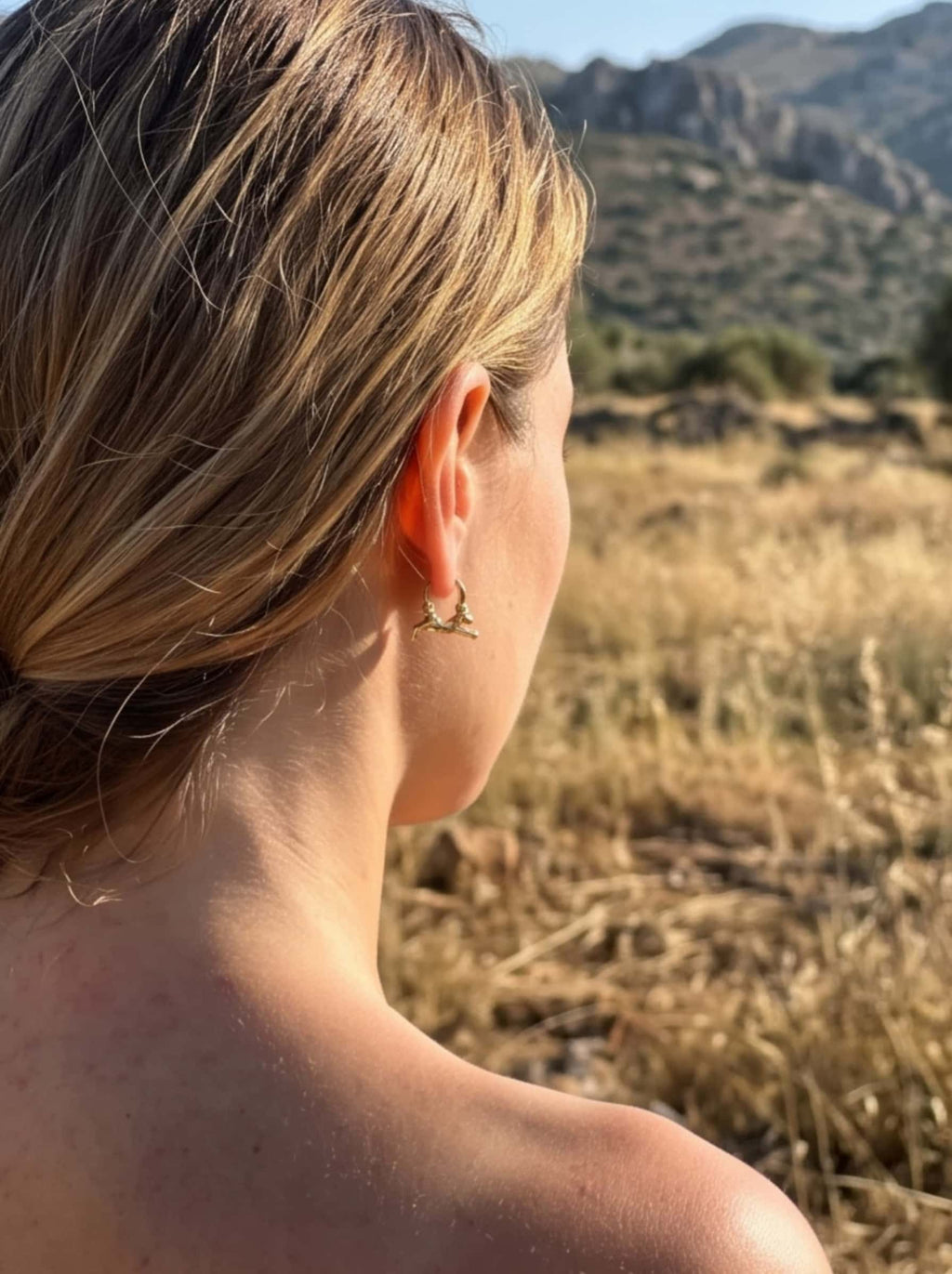 Outdoor lifestyle view of a woman wearing dainty gold cat earrings with an elegant updo