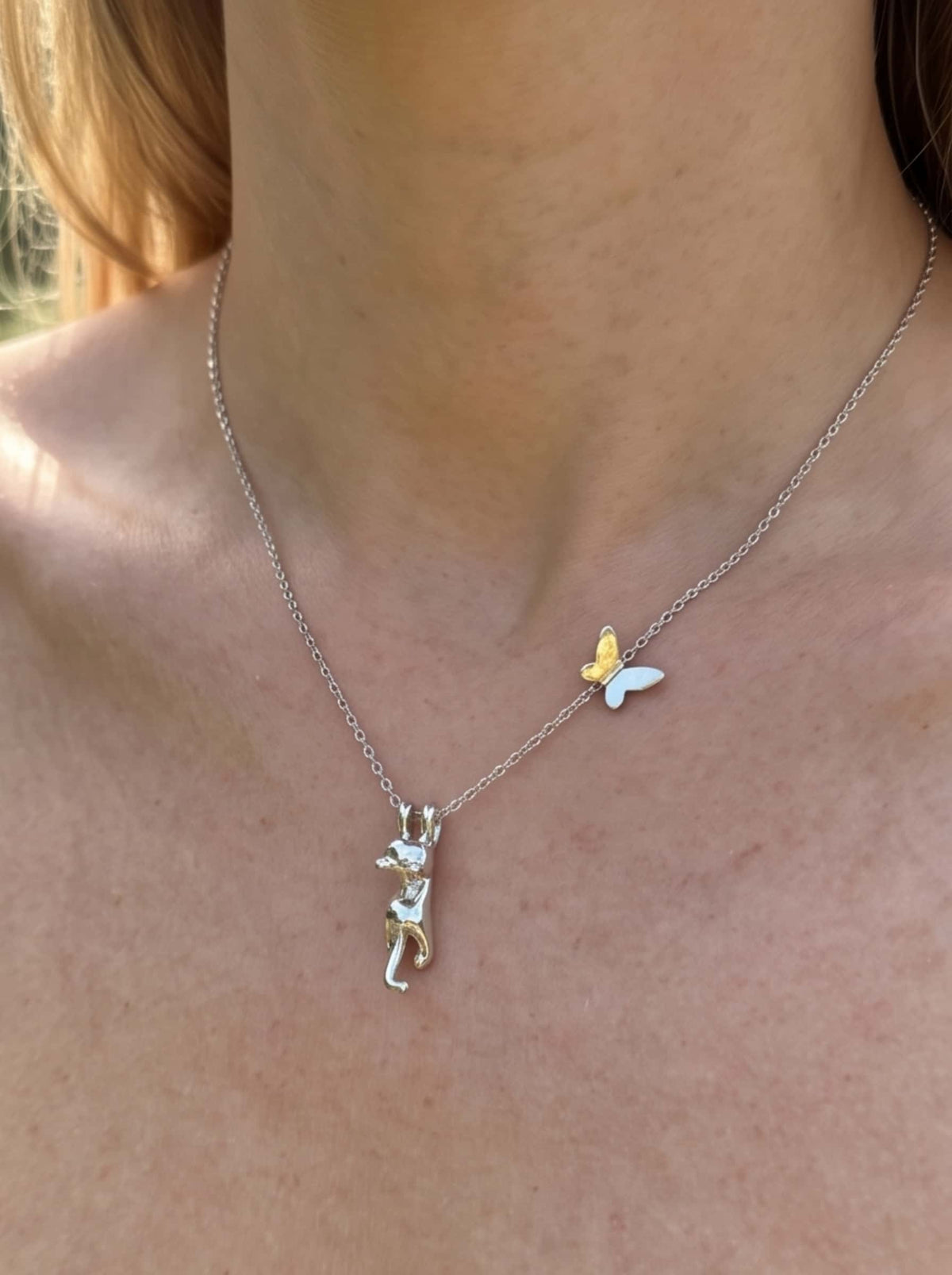 Close-up of a woman wearing the dainty cat pendant necklace, showing the detailed hanging cat charm and butterfly detail on the collarbone