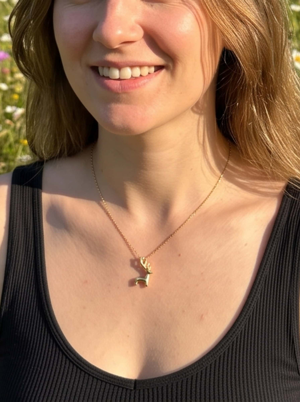 Smiling model wearing the dainty gold deer necklace outdoors in a meadow of wildflowers