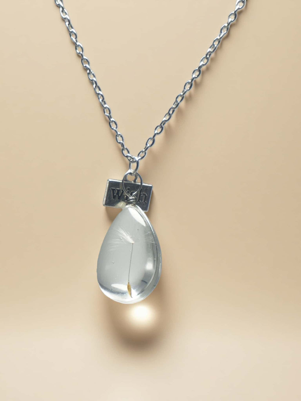 Teardrop-shaped pendant on a chain with a beige background