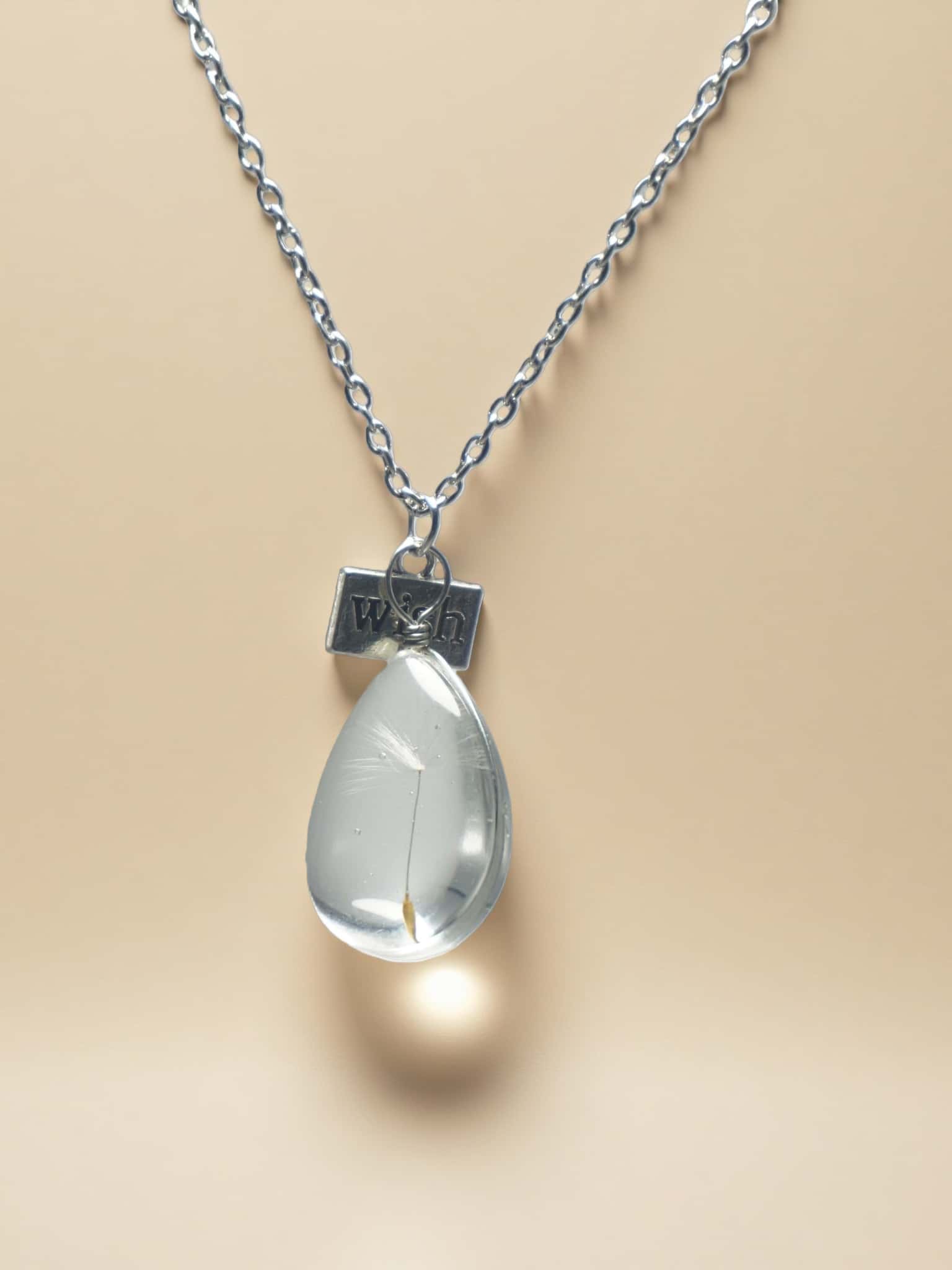 Teardrop-shaped pendant on a chain with a beige background