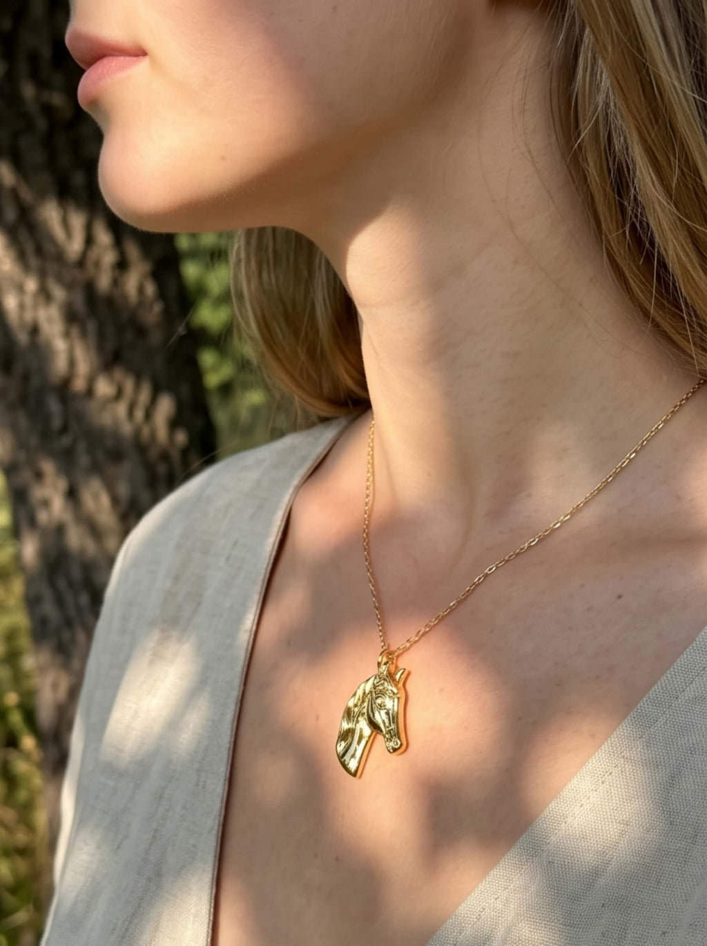 Side profile close-up of a female model wearing the detailed horse necklace during golden hour outdoors