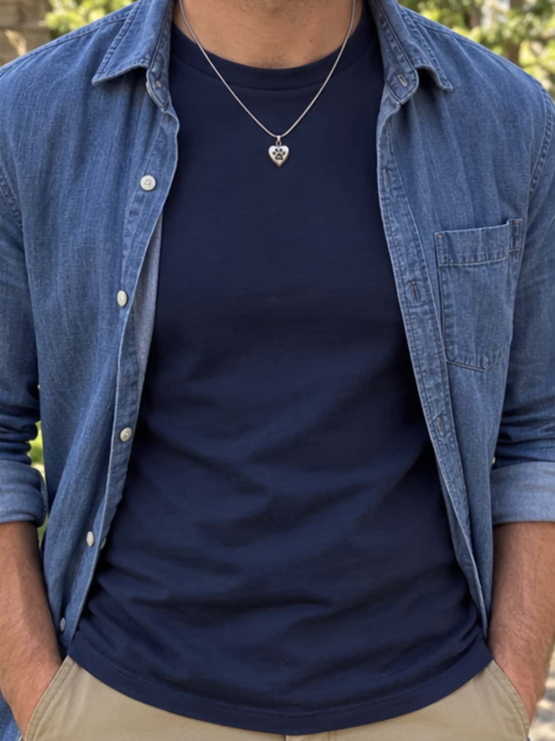 Man wearing a paw print heart dog ashes necklace with a navy T-shirt and blue denim shirt outdoors