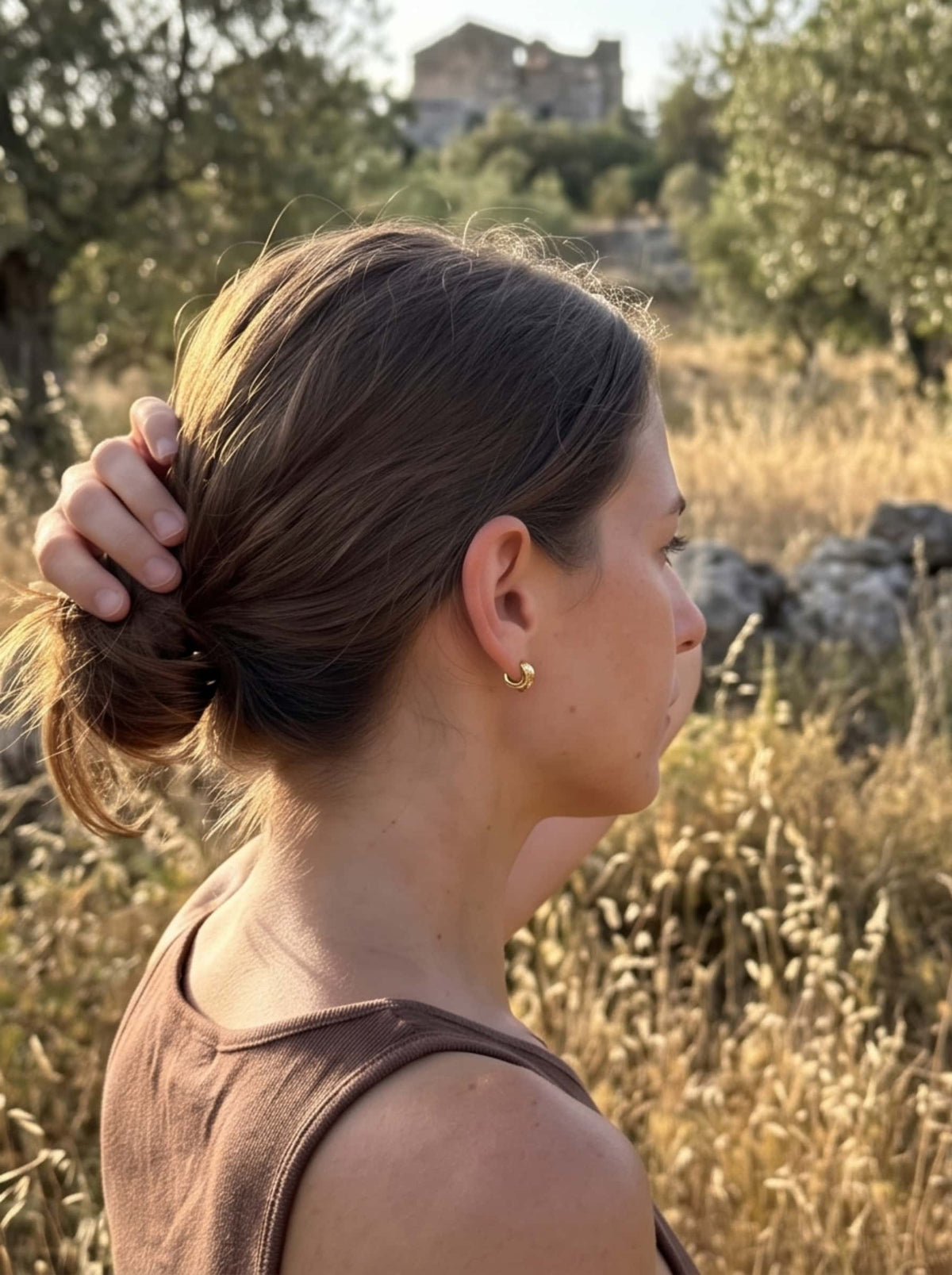 Model wearing delicate gold dog earrings outdoors under warm golden-hour natural light
